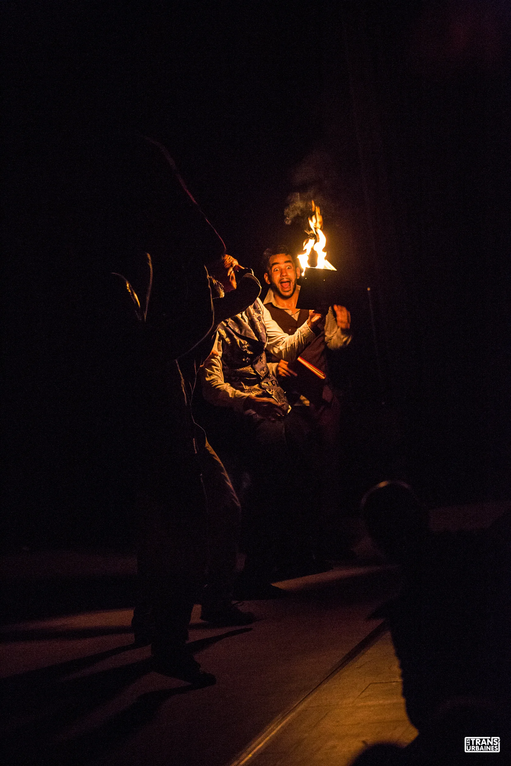 Groupe de personnes pratiquant la jonglerie avec des torches enflammées lors d'une performance nocturne, dans un environnement sombre.
