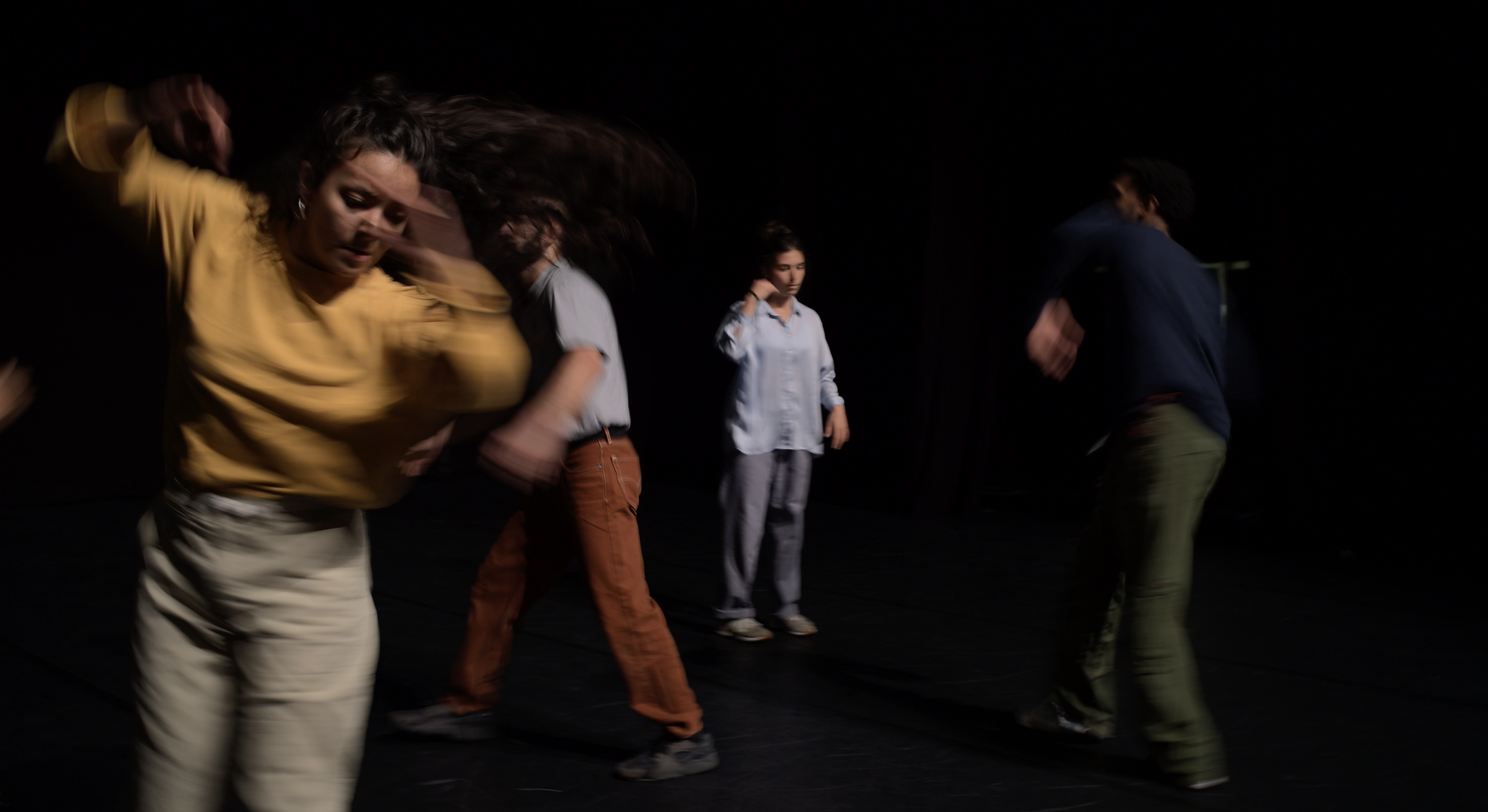 Groupe de quatre personnes dans une pièce sombre, en mouvement, certains avec des expressions concentrées.