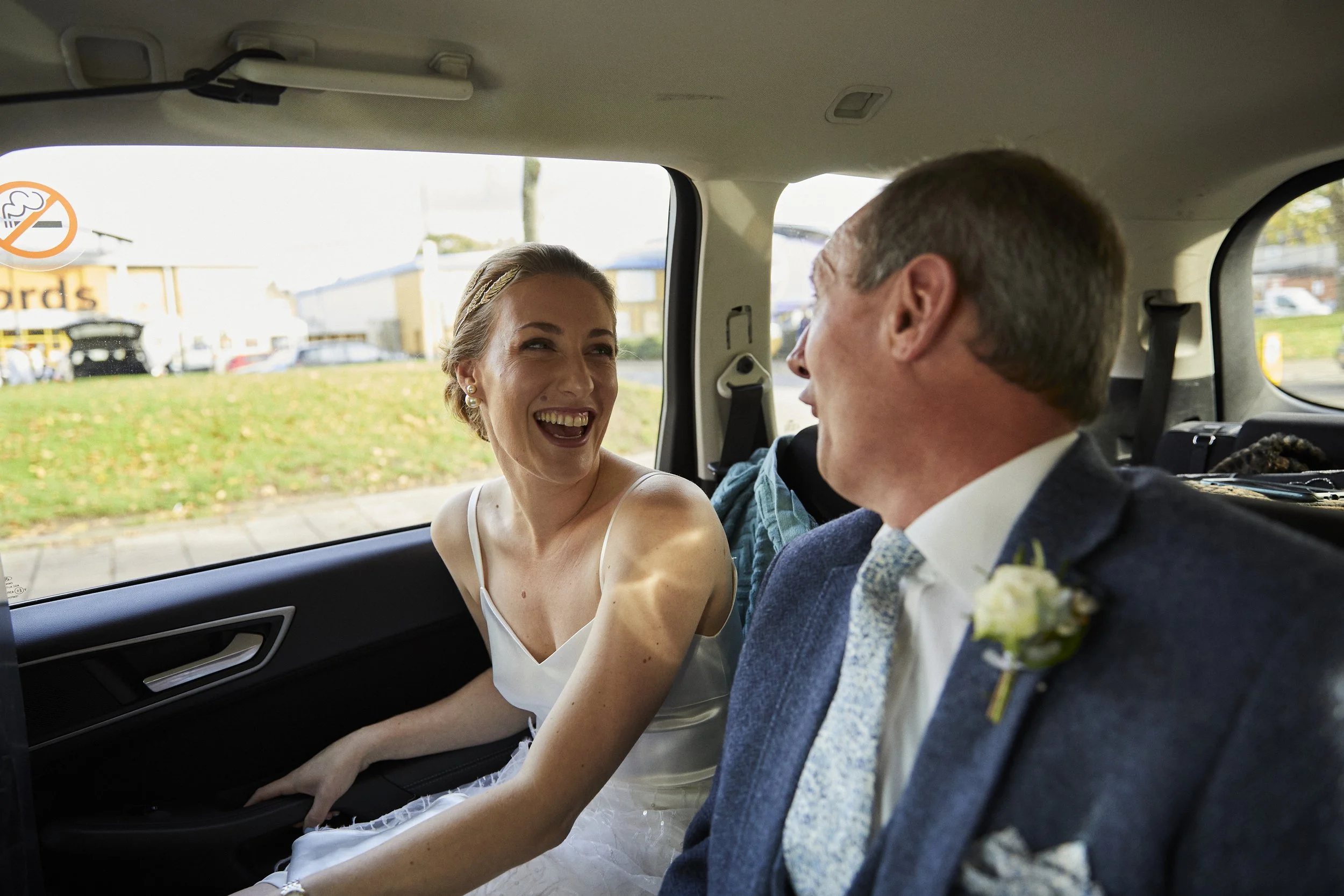 A bride and groom sitting together in the backseat of a vehicle, smiling and laughing on their wedding day.