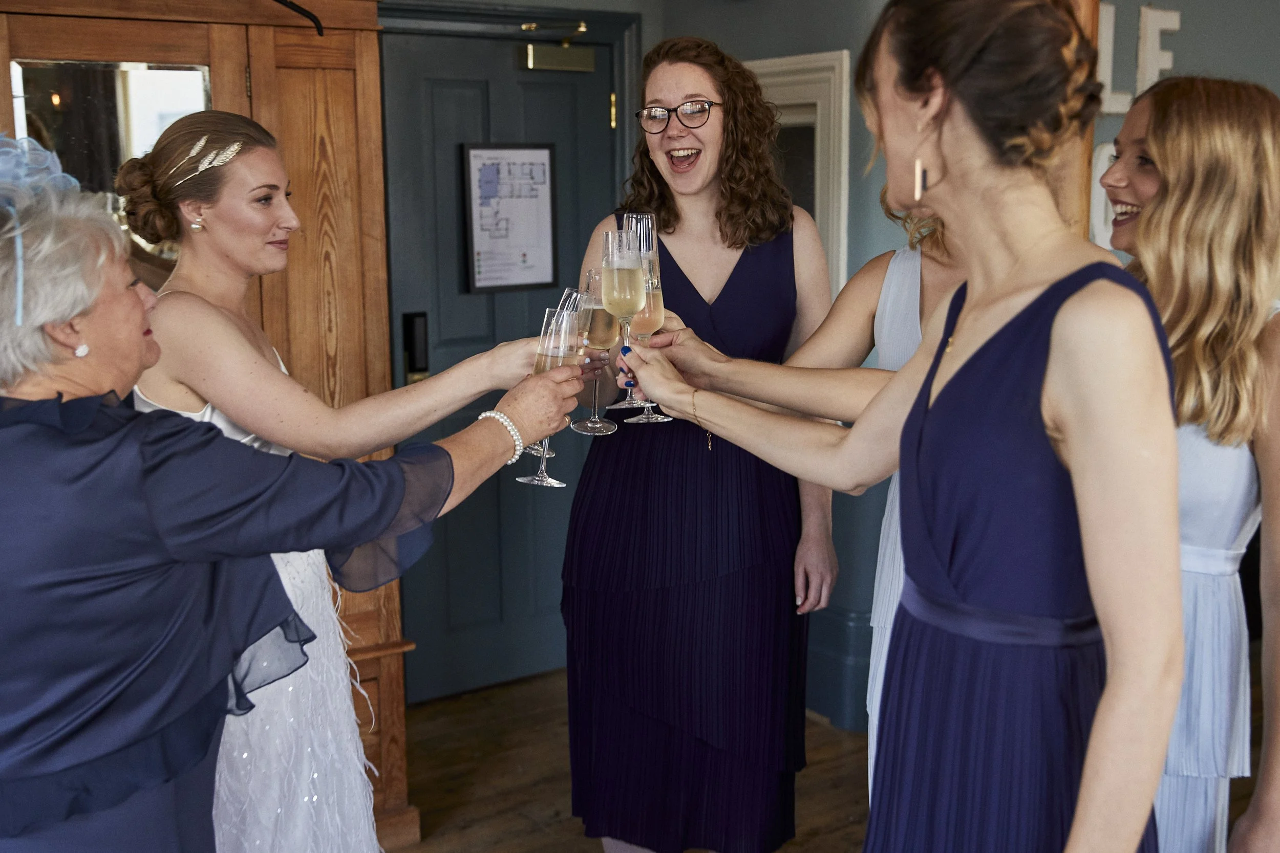 A group of women dressed in formal attire cheer and toast with glasses of champagne during a celebration in a cozy indoor setting.