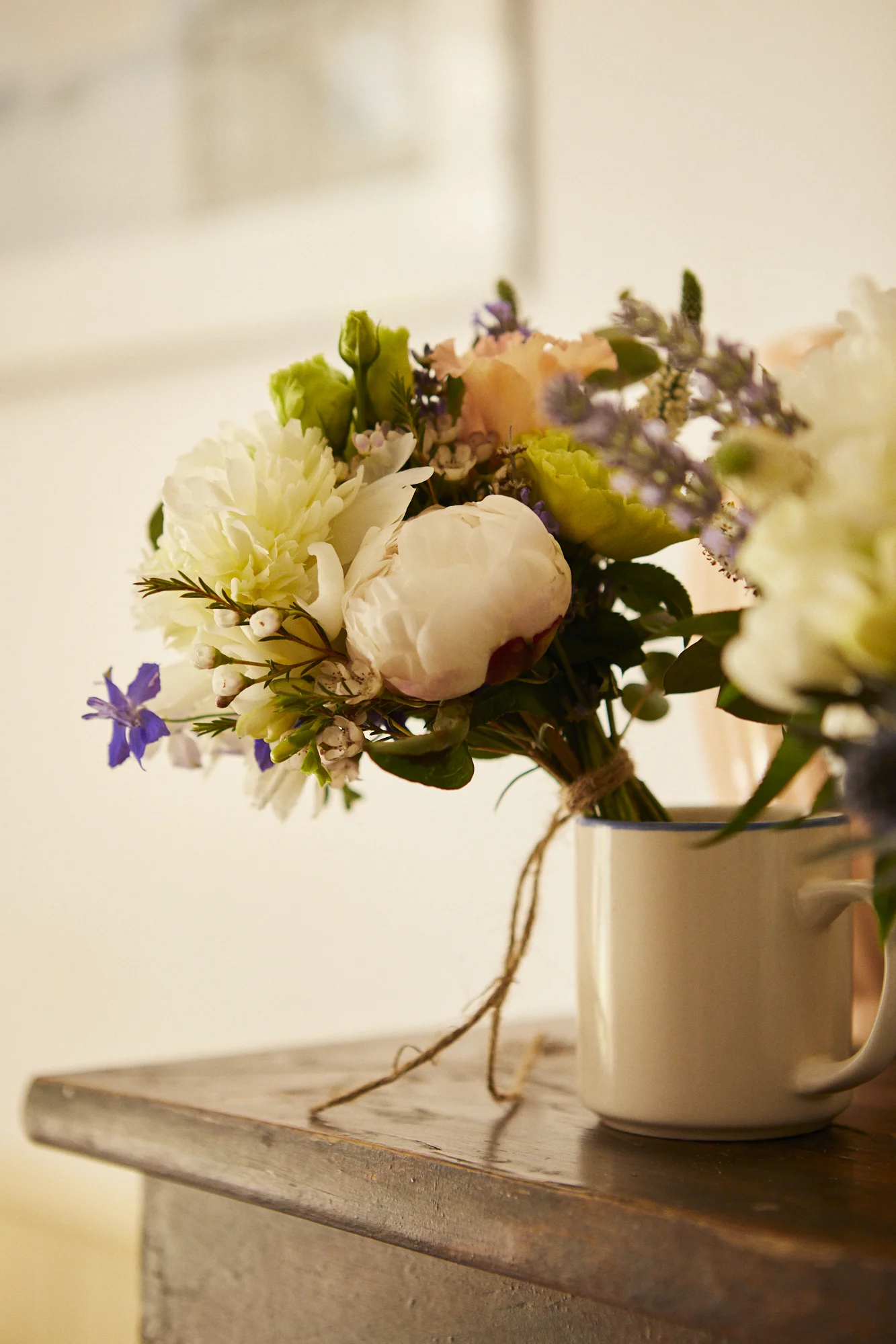 A bouquet of mixed flowers in a white mug sitting on a wooden surface.