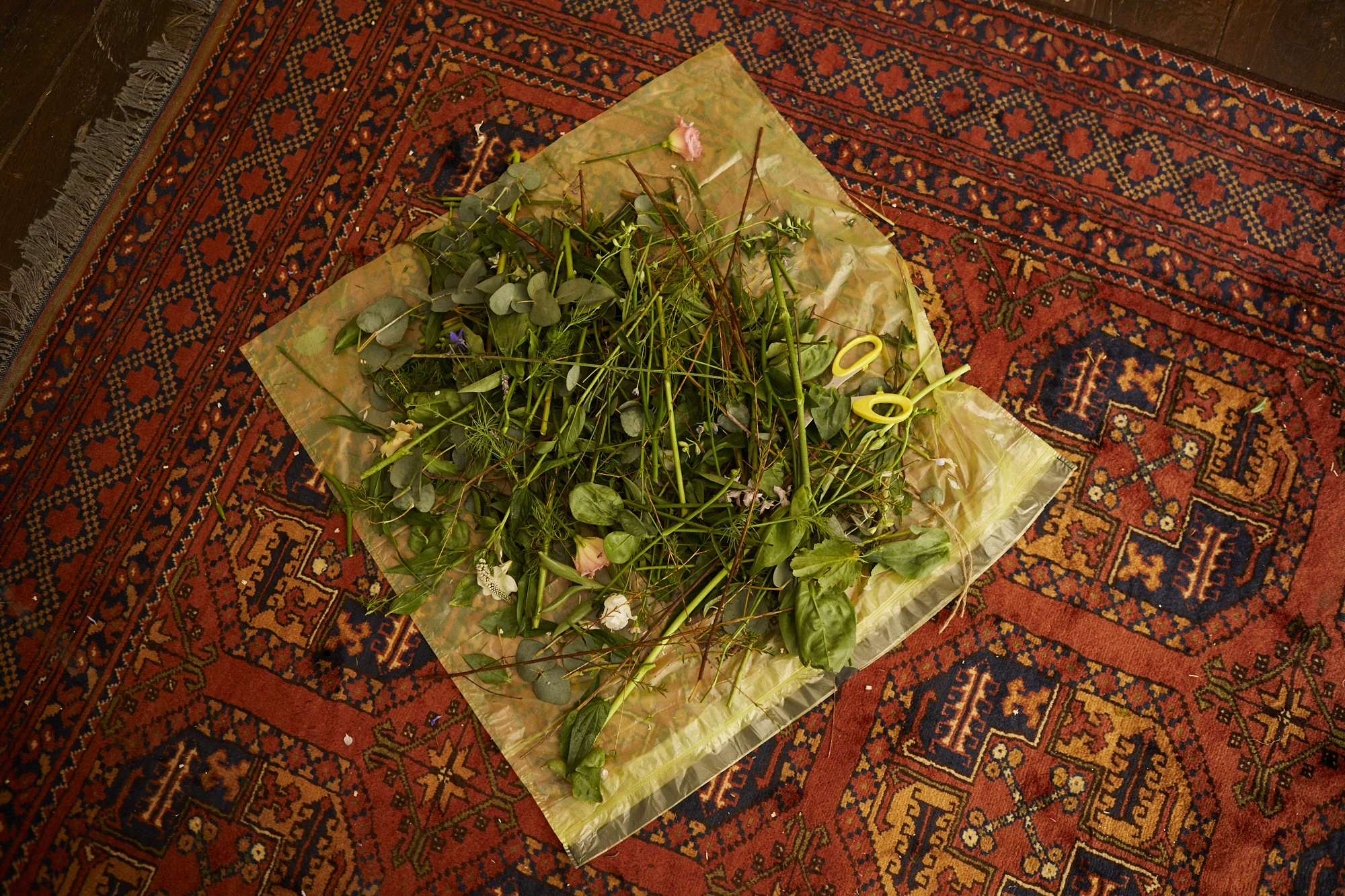 A pile of assorted flowers and greenery wrapped in transparent plastic on a patterned carpet.