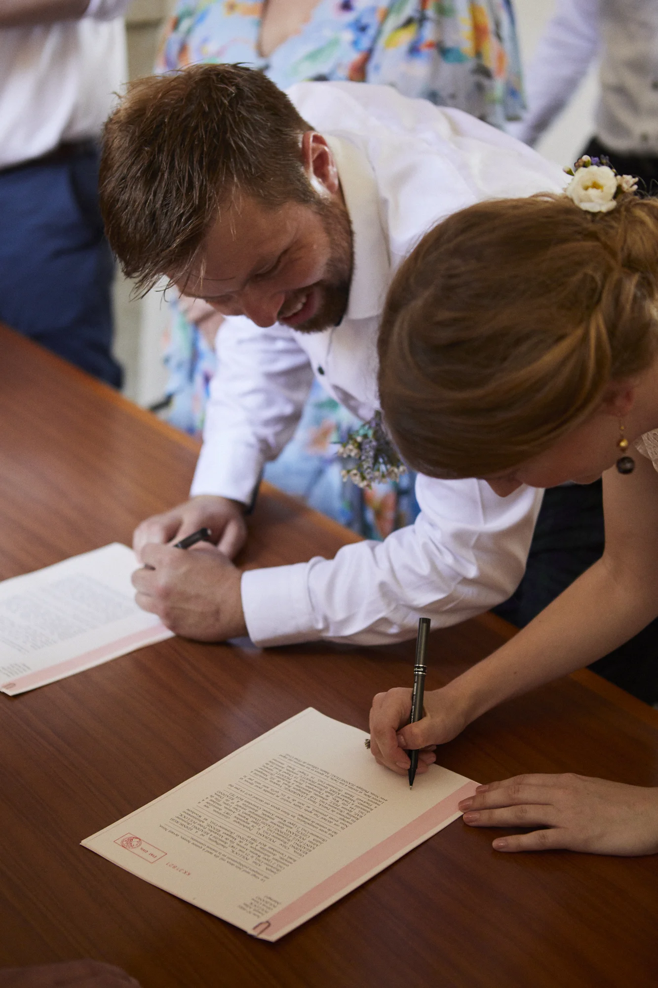 Two people signing documents on a wooden table during a ceremony or official signing event.