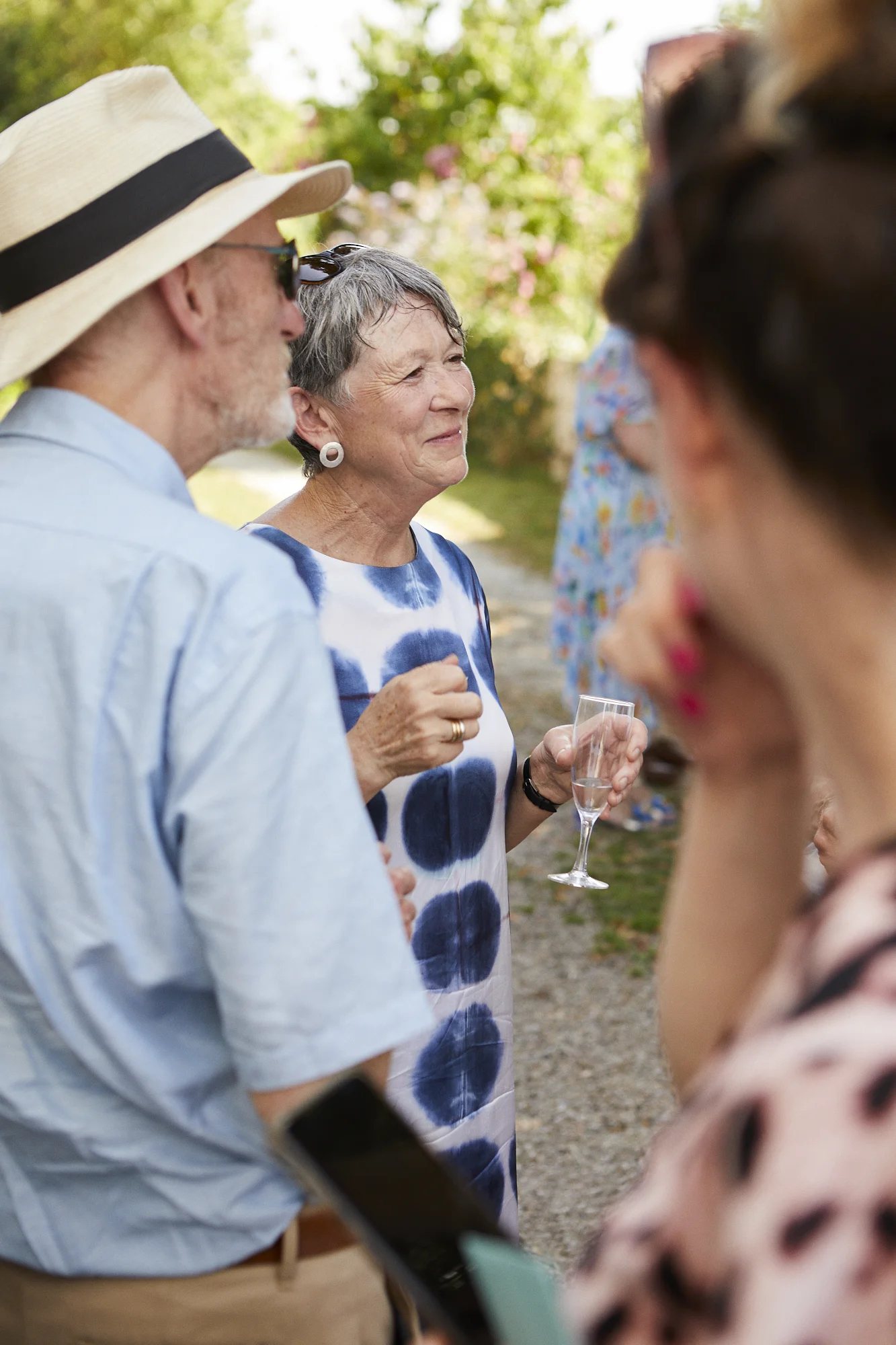 People socializing outdoors, woman holding a glass of champagne, trees in background