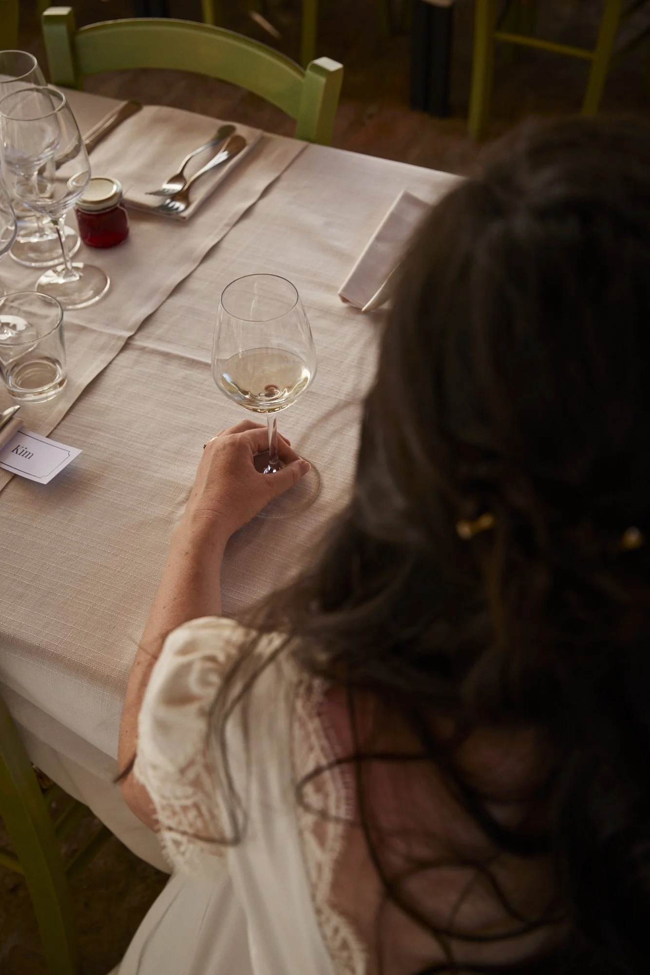 Person holding a wine glass at a dinner table set with glassware, silverware, and cloth napkins.
