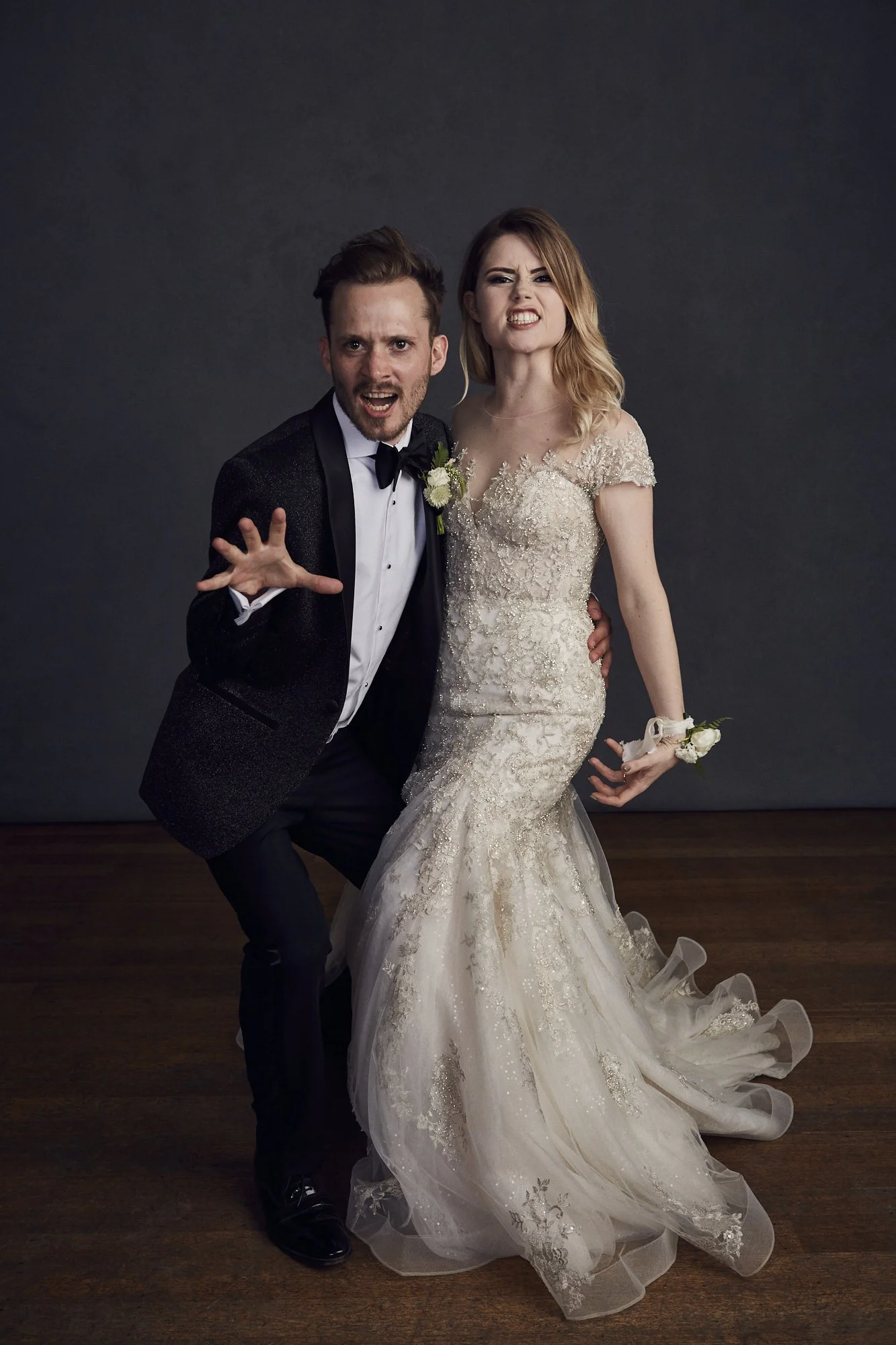 Man and woman in wedding attire making funny faces and posing playfully in a photography studio.