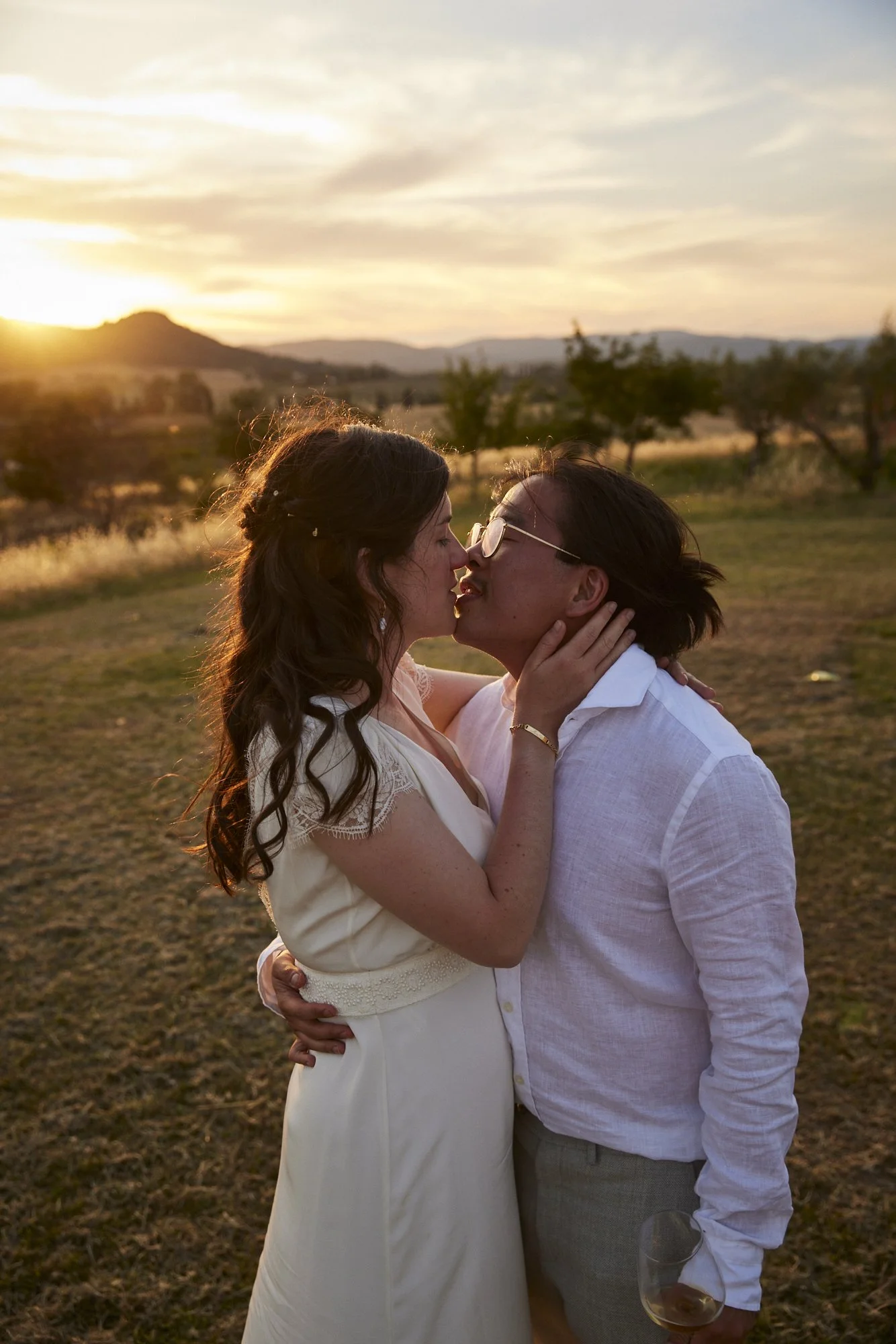 A couple kissing outdoors at sunset, with a scenic landscape in the background.