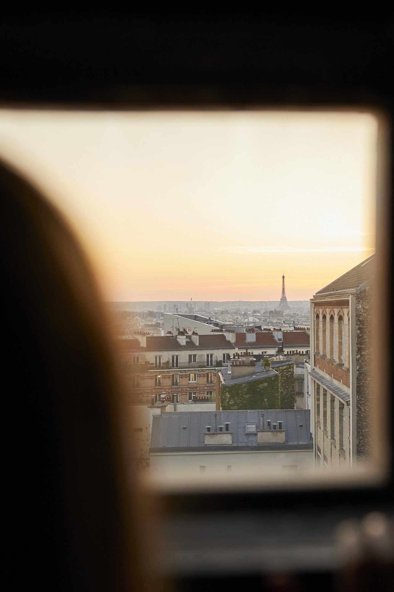 View of Paris skyline with Eiffel Tower at sunset, seen through a window.
