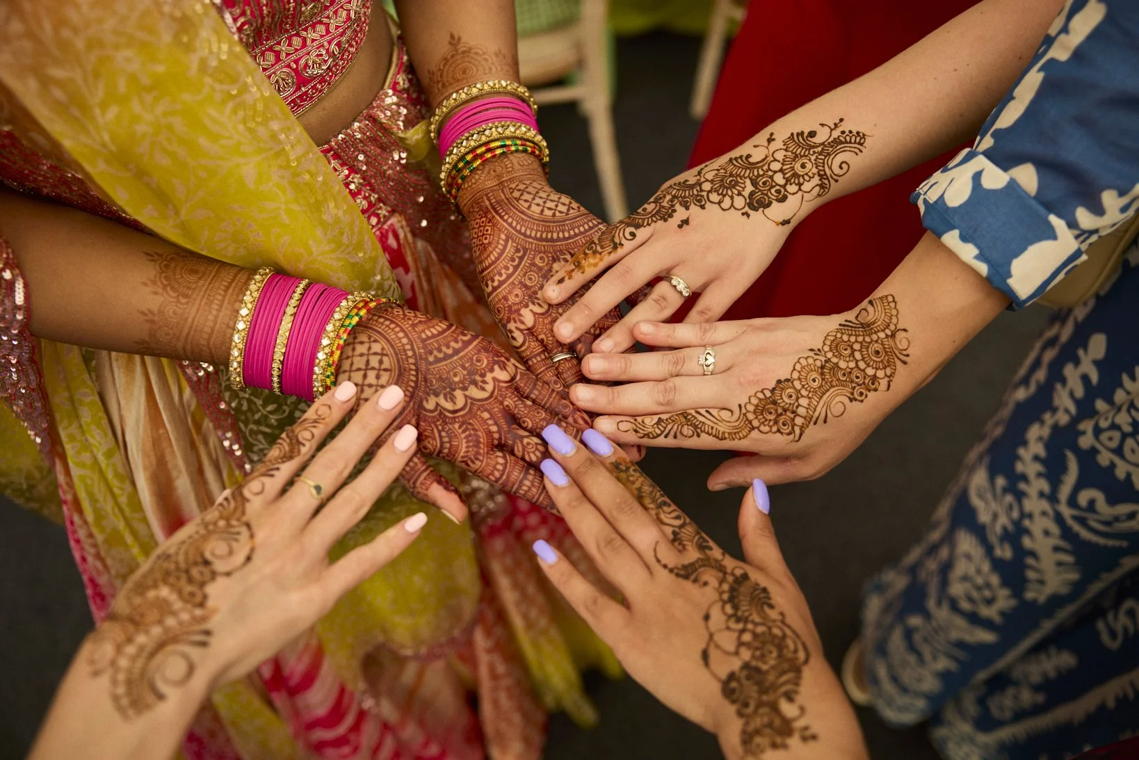 Multiple women showing their decorated hands with traditional henna designs at a celebration.
