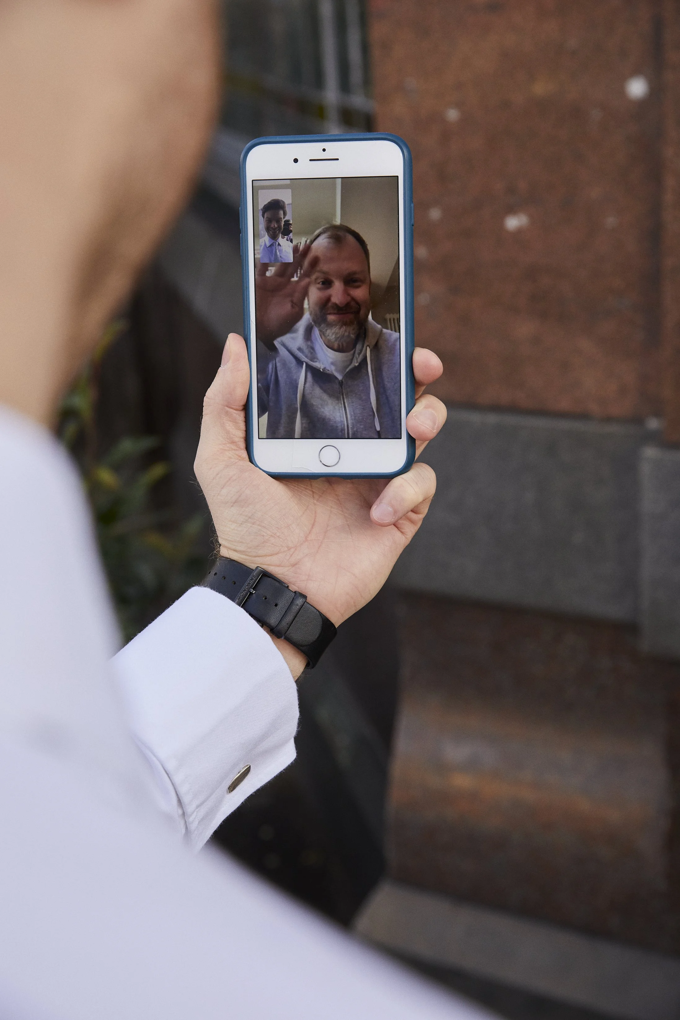 Person holding a smartphone taking a video call with a man waving and smiling.