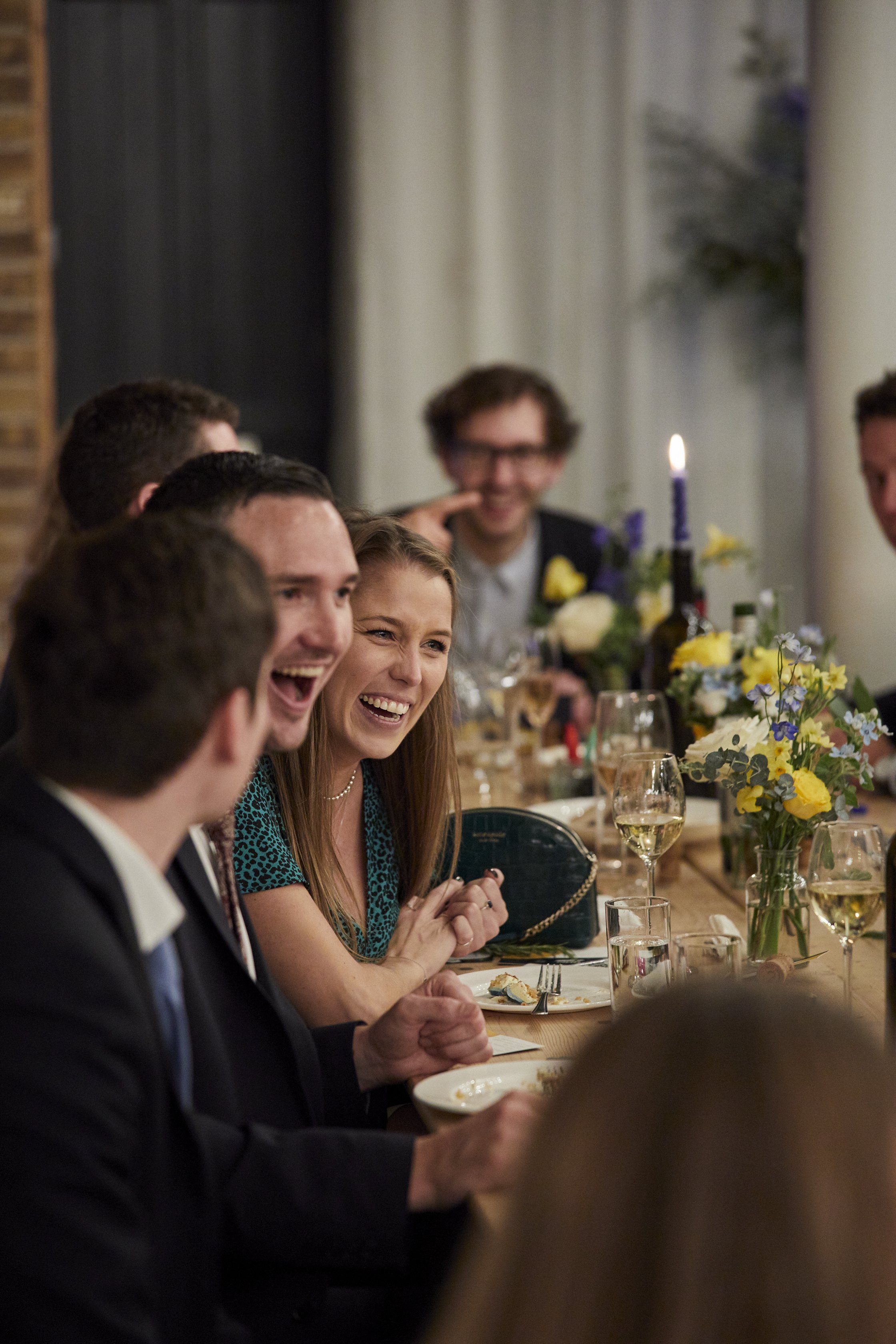 People enjoying a laughter-filled dinner party at a long table decorated with flowers.