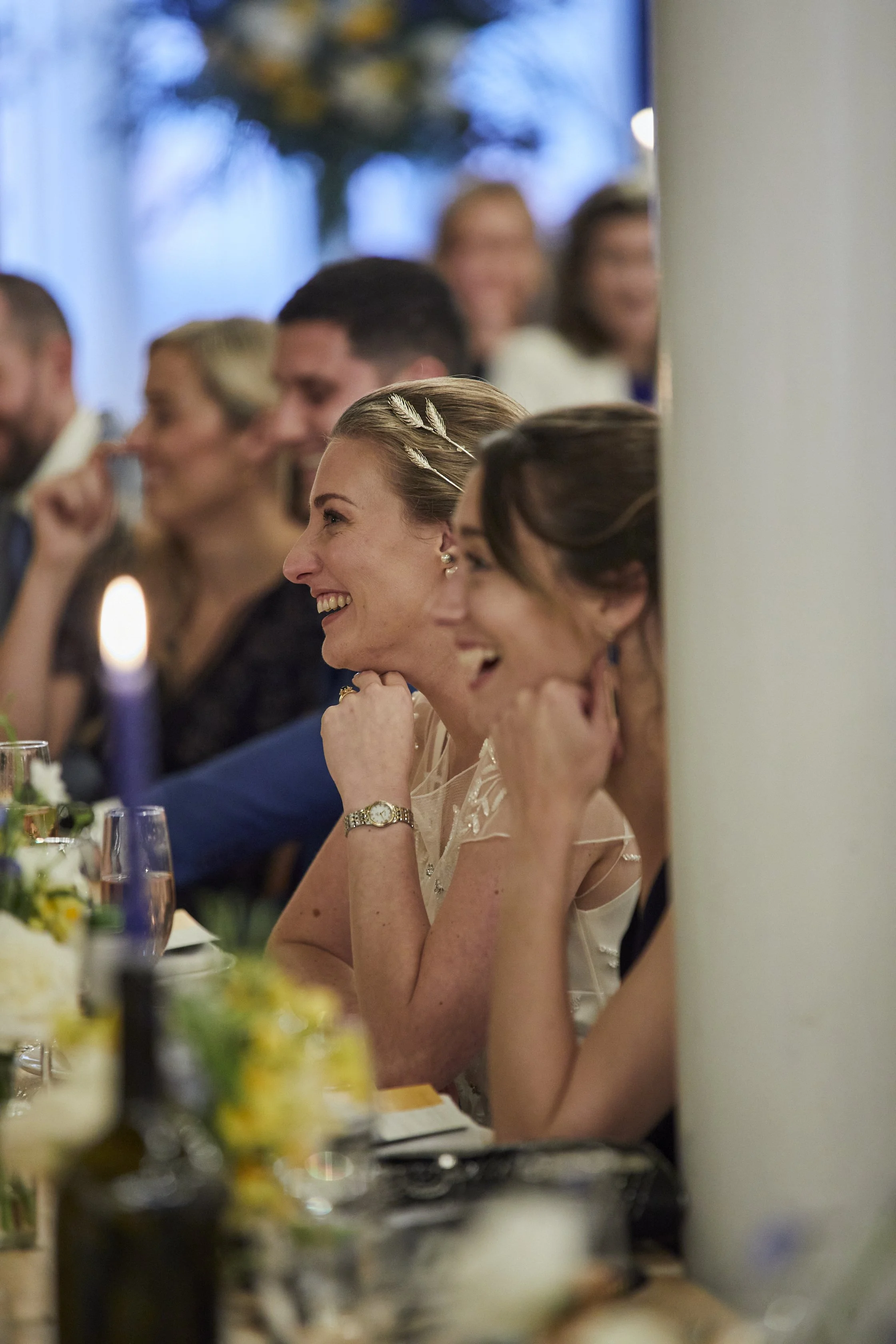 A group of people sitting at a table during a celebration, likely a wedding reception, smiling and engaging with the event.
