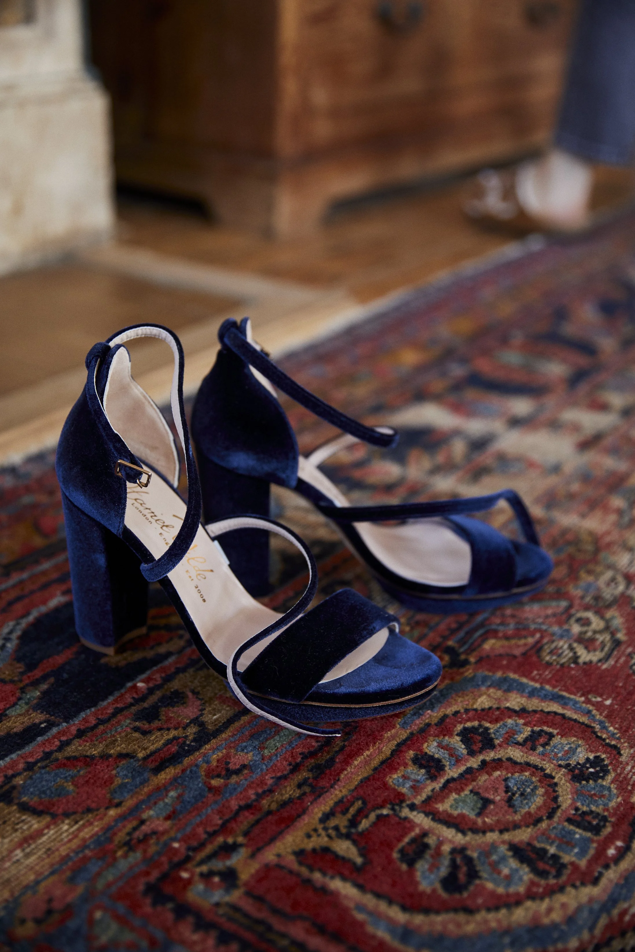 A pair of navy blue high-heeled sandals with ankle straps resting on a patterned rug.