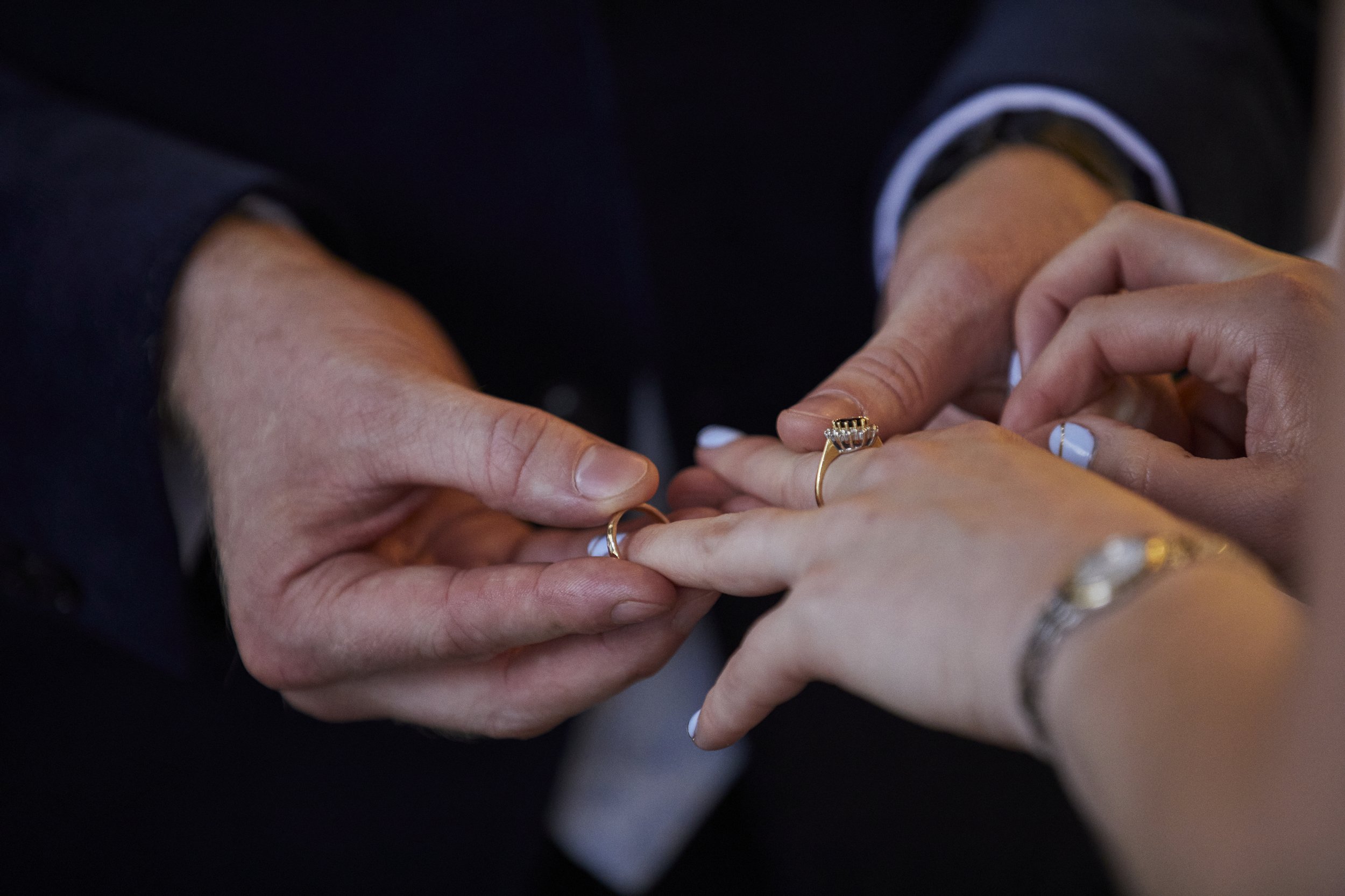 Someone holding a ring in front of another person's hand, with the person wearing multiple rings, in a close-up shot.