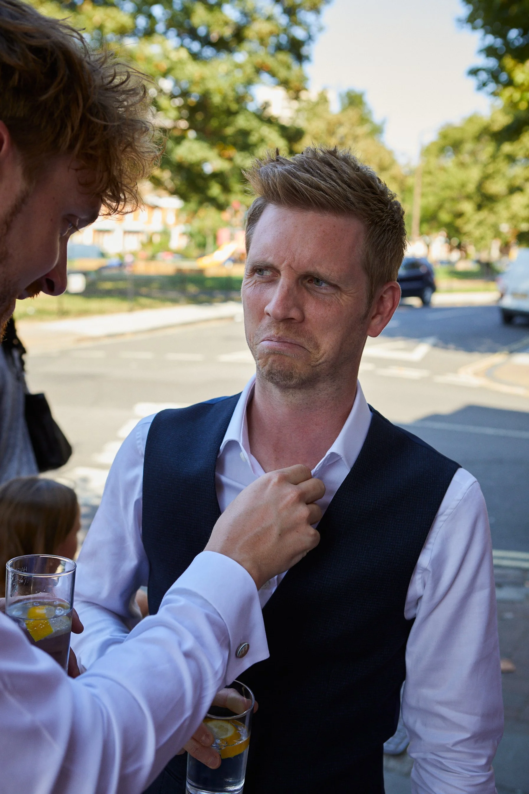 A man in a white shirt and vest making a disapproving or confused facial expression while looking at another person.