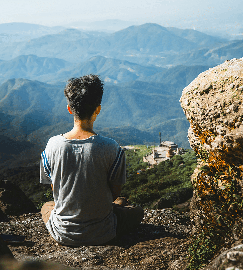 Person sitting outdoors overlooking mountains, reflecting during eating disorder recovery and online therapy support
