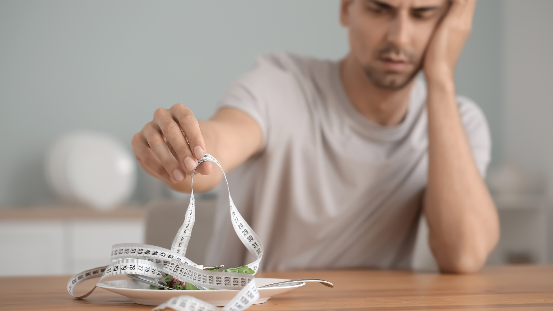 Man stares at a measuring tape and vegetables on a plate. Begin online eating disorder therapy in San Jose, California at Kindful Body.