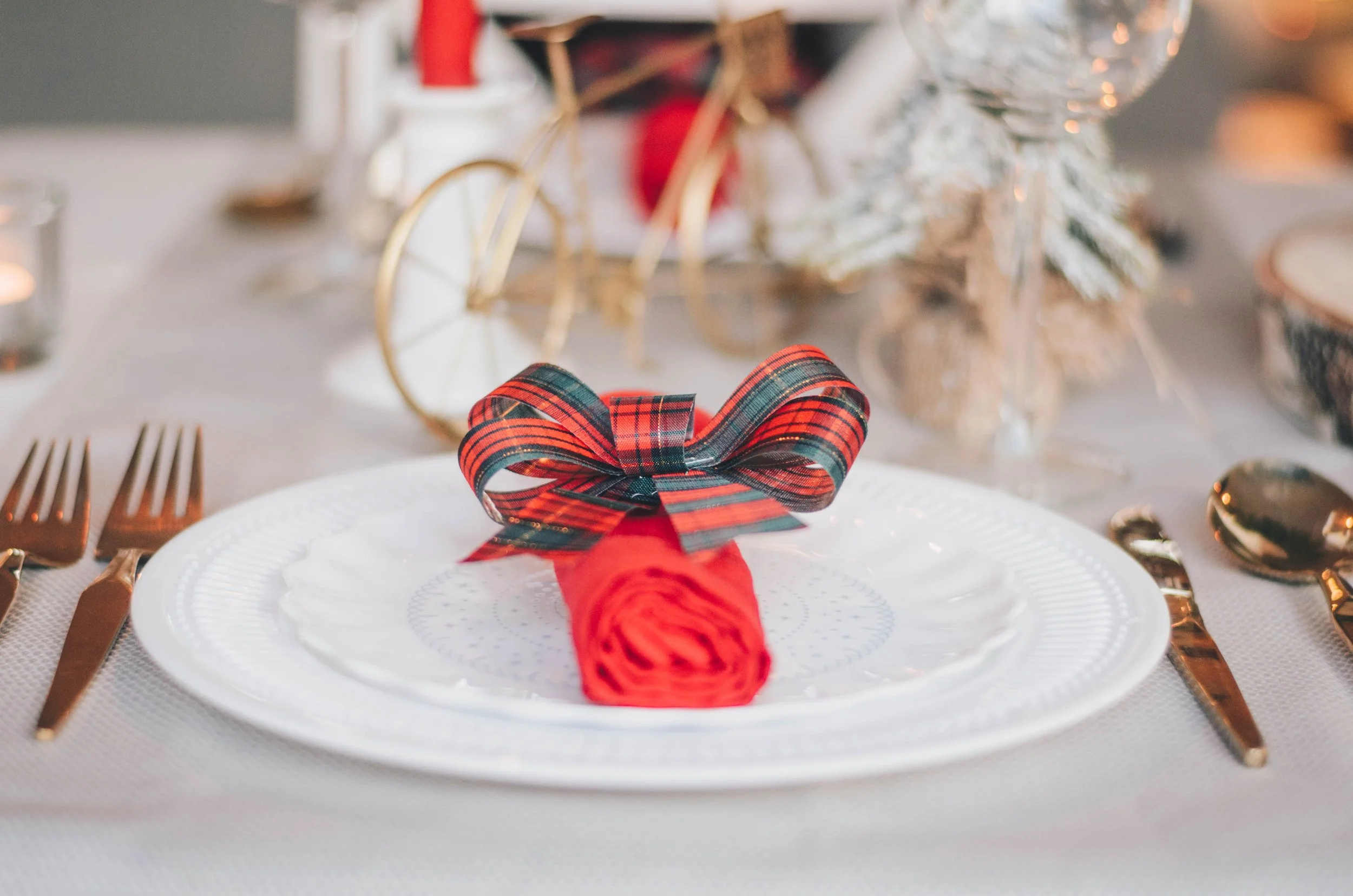 A Christmas dinner table place setting with a red napkin tied with a bow.