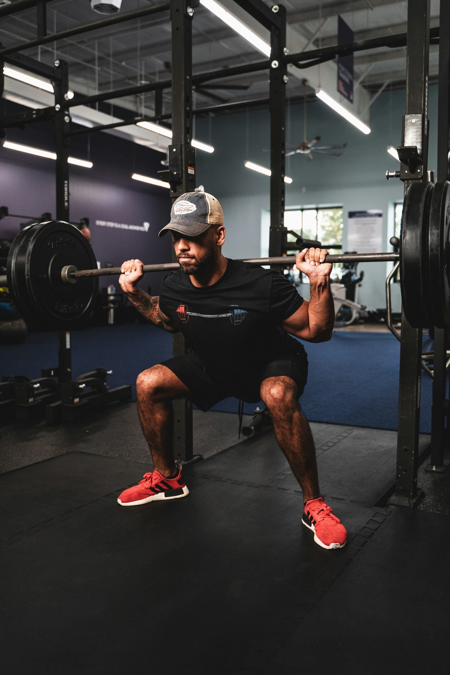Man performing a weighted squat in a gym, focused and strong—representing intentional movement and redefining strength through a recovery-informed lens.
