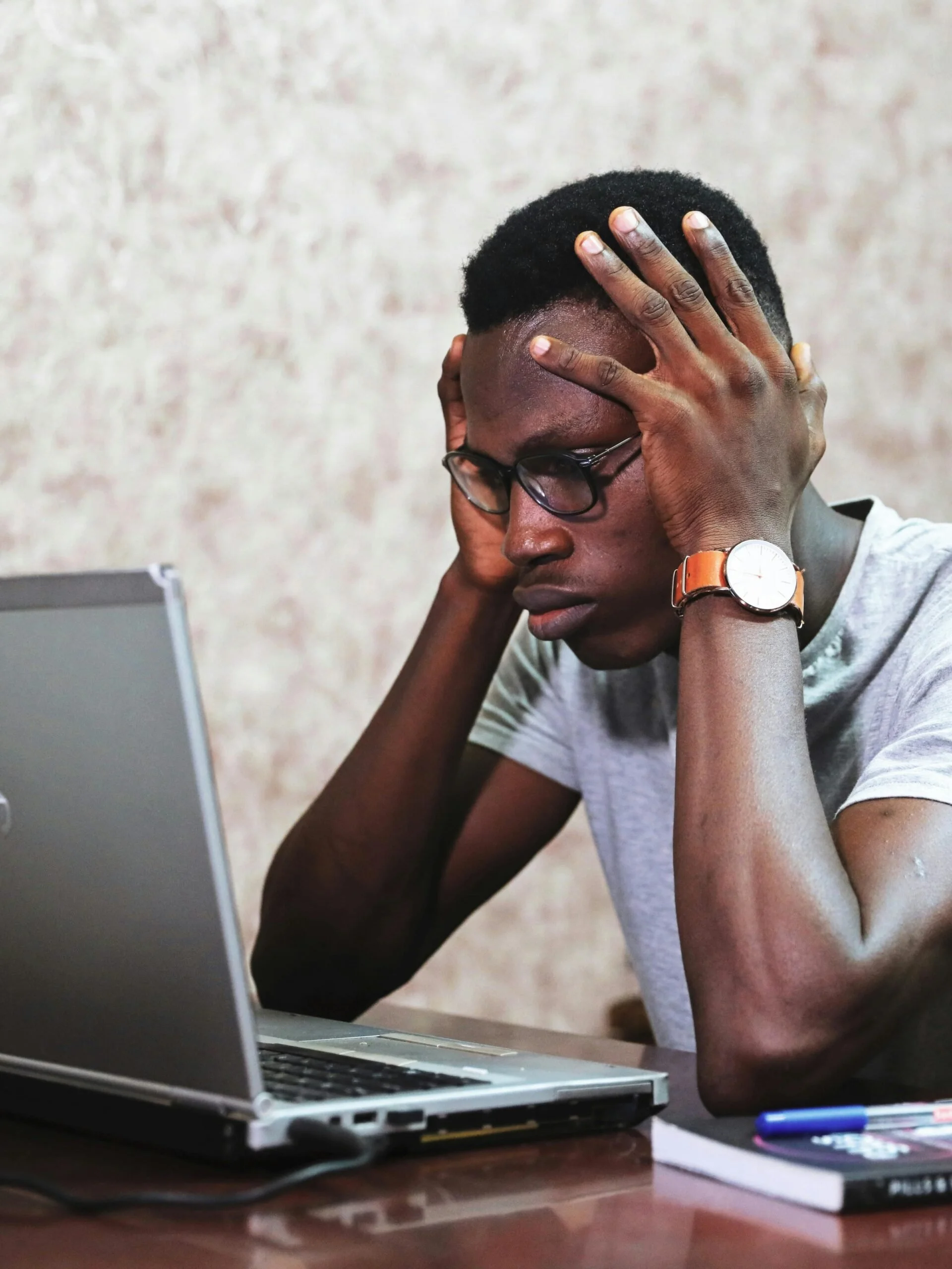 Young man sitting at a desk with his hands on his head, looking overwhelmed while staring at a laptop—symbolizing the emotional and cognitive toll of disordered eating, stress, or body image pressure.