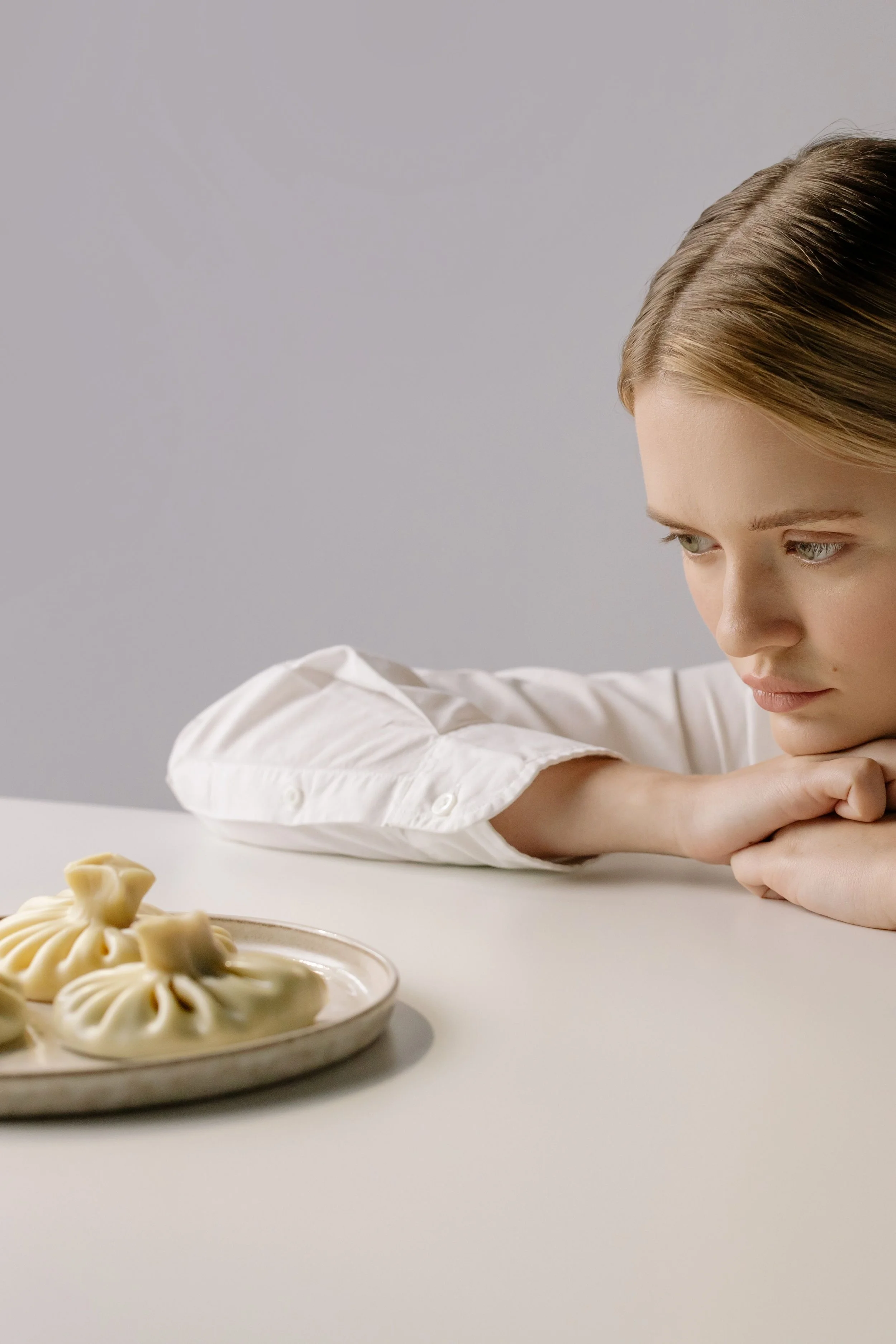 Young person staring anxiously at a plate of food, illustrating food avoidance and restrictive eating behaviors associated with atypical eating disorders.