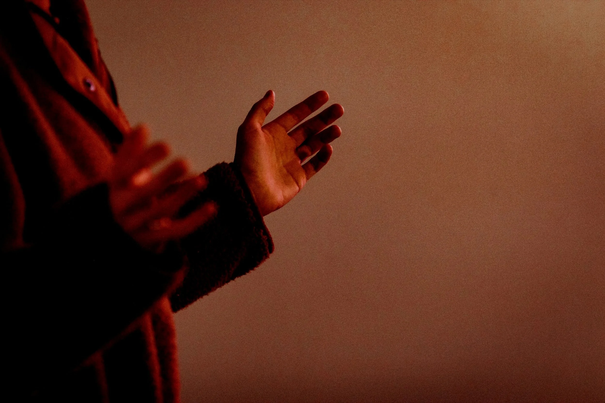 A person's hand raised against a plain wall, with warm lighting creating a silhouette effect.