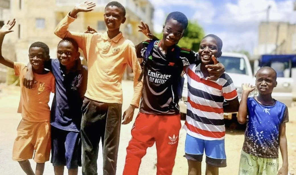 A group phto with 6 young boys waving and smiling at the camera