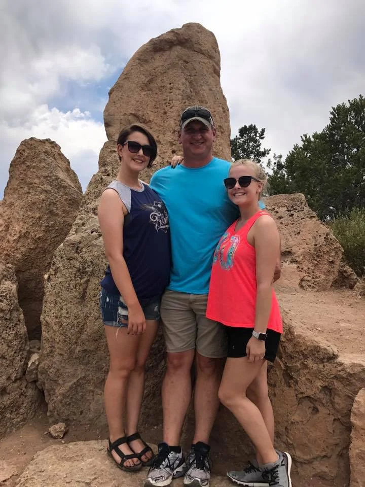 Shot of father and two daughters standing in front of rock formations.