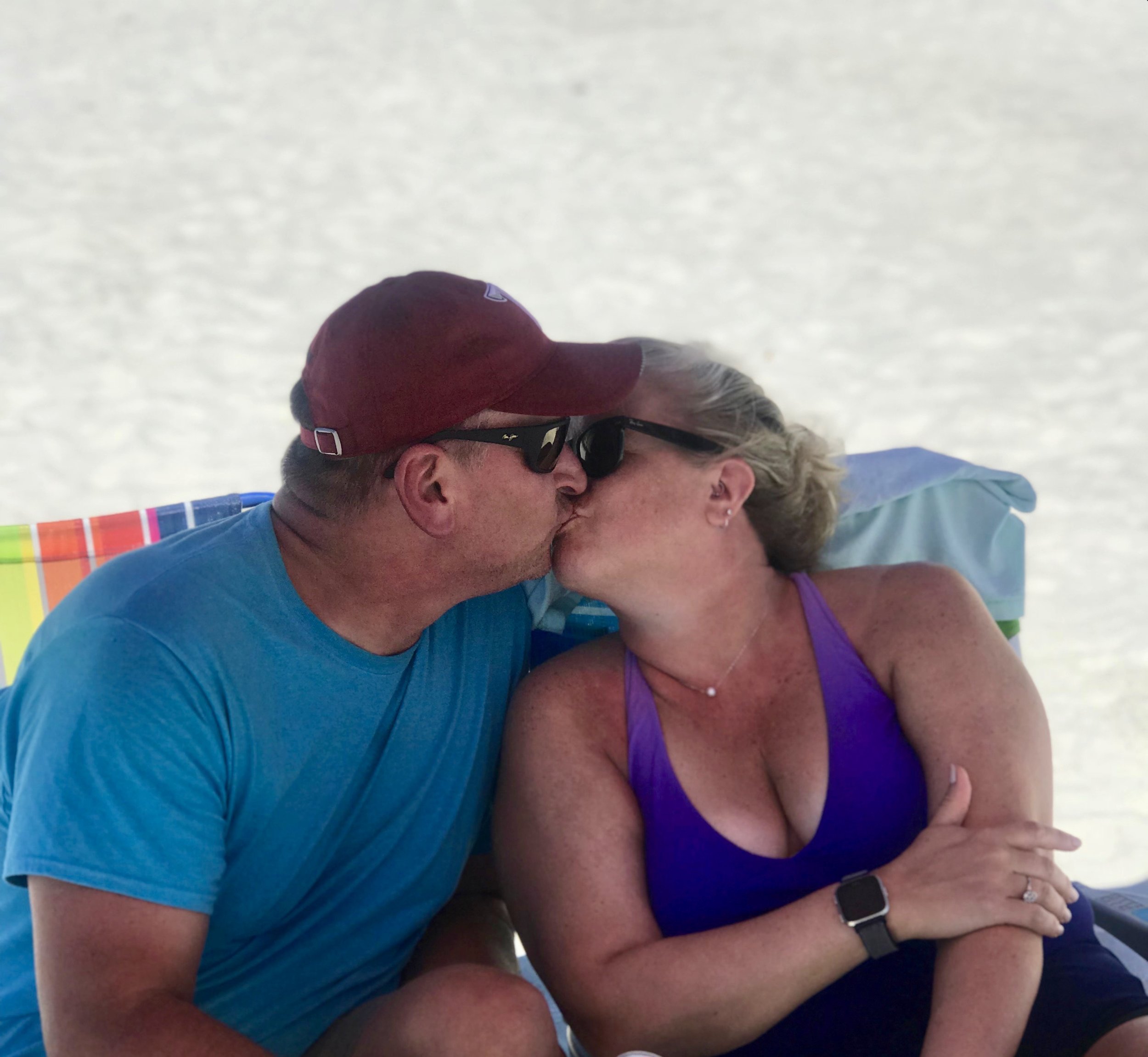 Danny and Brooke kissing on beach while sitting in beach chairs.
