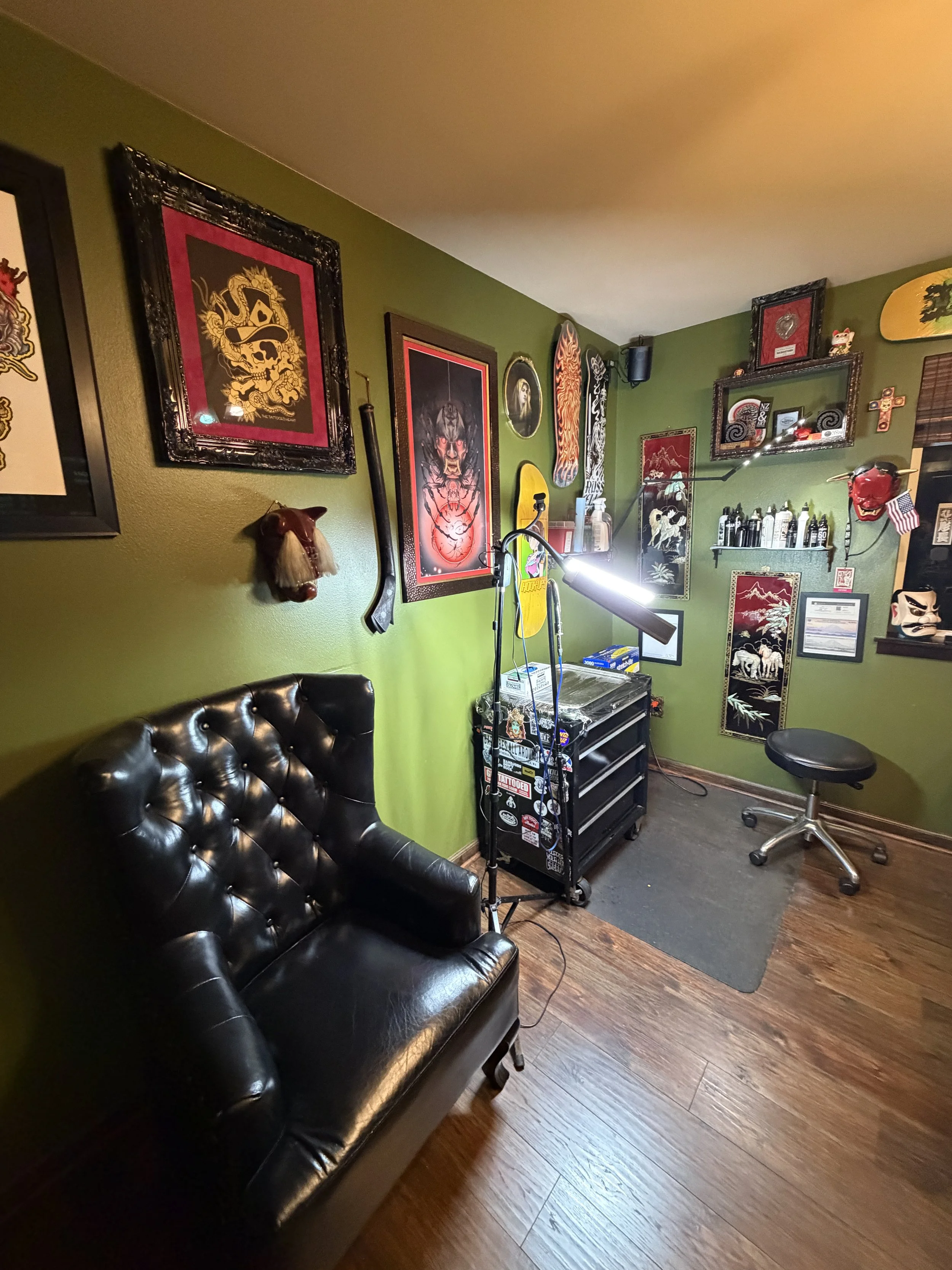 Private tattoo studio interior in Seattle featuring a luxury black leather tufted armchair, olive green walls adorned with artwork, and a professional tattoo workstation.