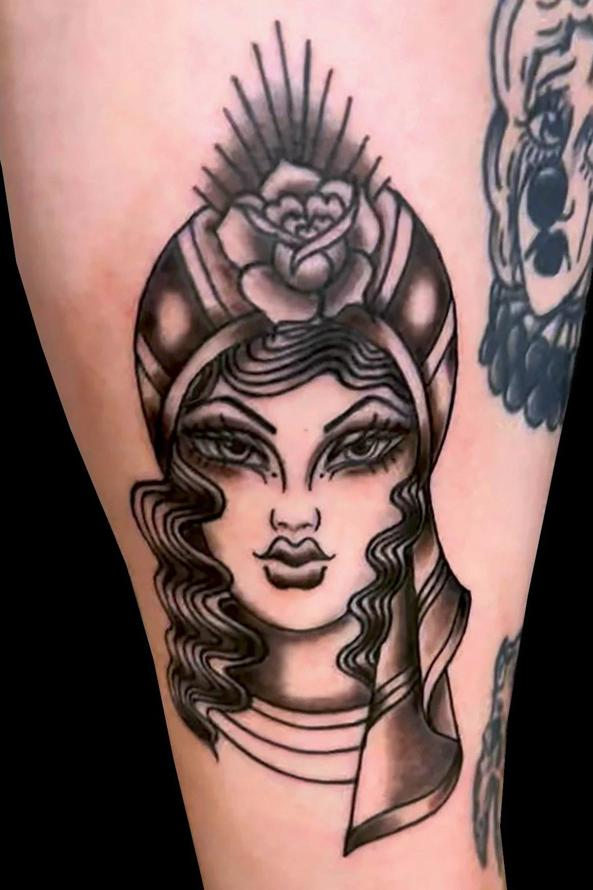 A detailed black and gray tattoo portrait of a woman's face with a decorative rose nestled in her stylized hair.