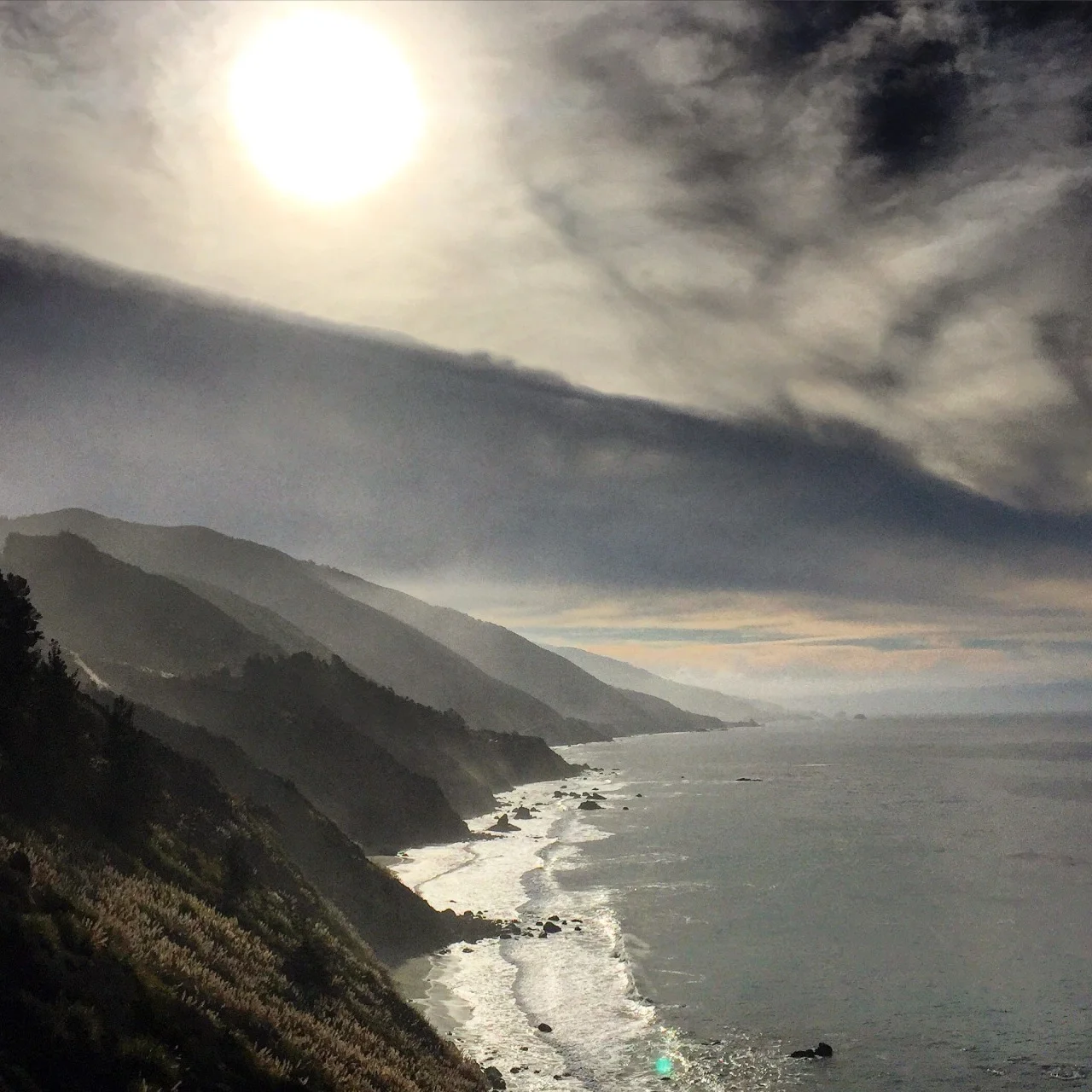 It makes one feel very small to wait for a whale. Almost an hour spent on a sheer cliff, looking out to sea, like an anxious child waiting for a circus act to begin. The tent now is the Pacific Coast Highway, its big top extending as far west as the eye sees. The whales’ annual migration from Alaska to Mexico occasions a winter pilgrimage to Big Sur to witness their great girths slowly gliding southward.
Binoculars resting on the hood of the car, I quieted the engine and the music, listening to the rush of the wind, the rough surf endlessly pounding the rocks below. Too far up to hear the whales exhale, I surely could see their spouts blow high in the air.
It is within nature my voice is heard by my heart; where creativity breathes; where my innate individuality is woven into the vibrant fabric of the planet. Living amongst others in densely populated sub-urbanity, my humanity tugs, begging me to grasp, or at least glimpse, the true notions of compassion, empathy. My lacking efforts are too often made with wide eyes and mouth agape. There are so many people now, nosily clamoring for attention in ways sometimes grotesque. The crowded ugliness suffocates. But pulling into a state park along the coast moments before sunset accompanied by the soulful horn of Miles Davis, I’m the only one on Earth. The sky changes with each passing moment, reflecting off the glistening coats of black cows grazing on nearby hills now saturated in pastels. Vigor and peace are restored while watching dusk negotiate terms with day and night, its flamboyant hues those found in a child’s watercolor.
#california #bigsur #whalewatching