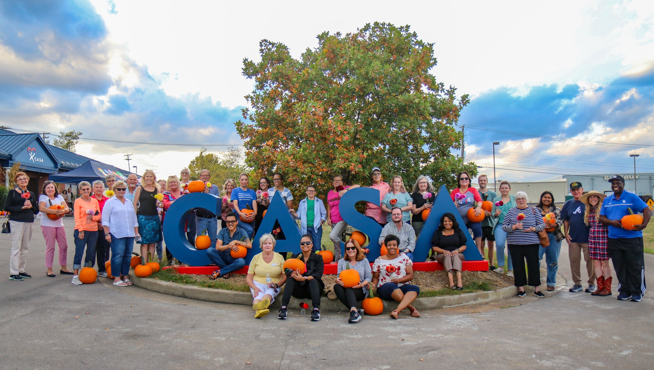CASA volunteers, staff and board members pose with pumpkins around the CASA monument at the 2023 Fall Festival volunteer appreciation event.