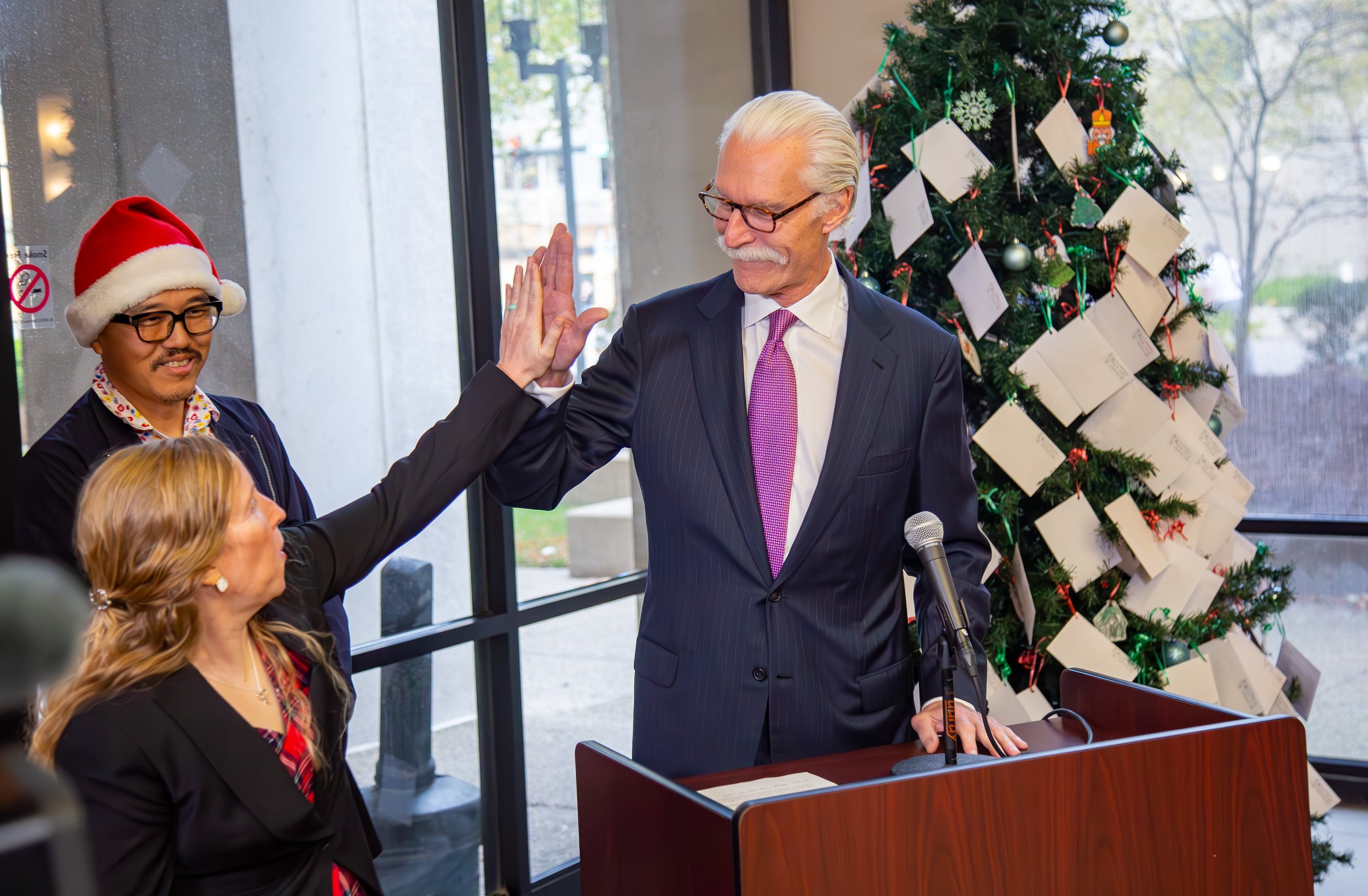 McBrayer Law Firm Managing Member James H. Frazier III high-fives CASA of Lexington Executive Director Melynda Jamison during the 2024 Fayette County CASA Angel Tree lighting at McBrayer.
