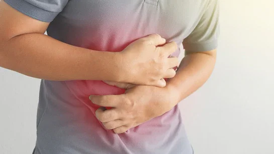 A modern building on a green hillside with snow-capped mountains in the background under a cloudy sky.