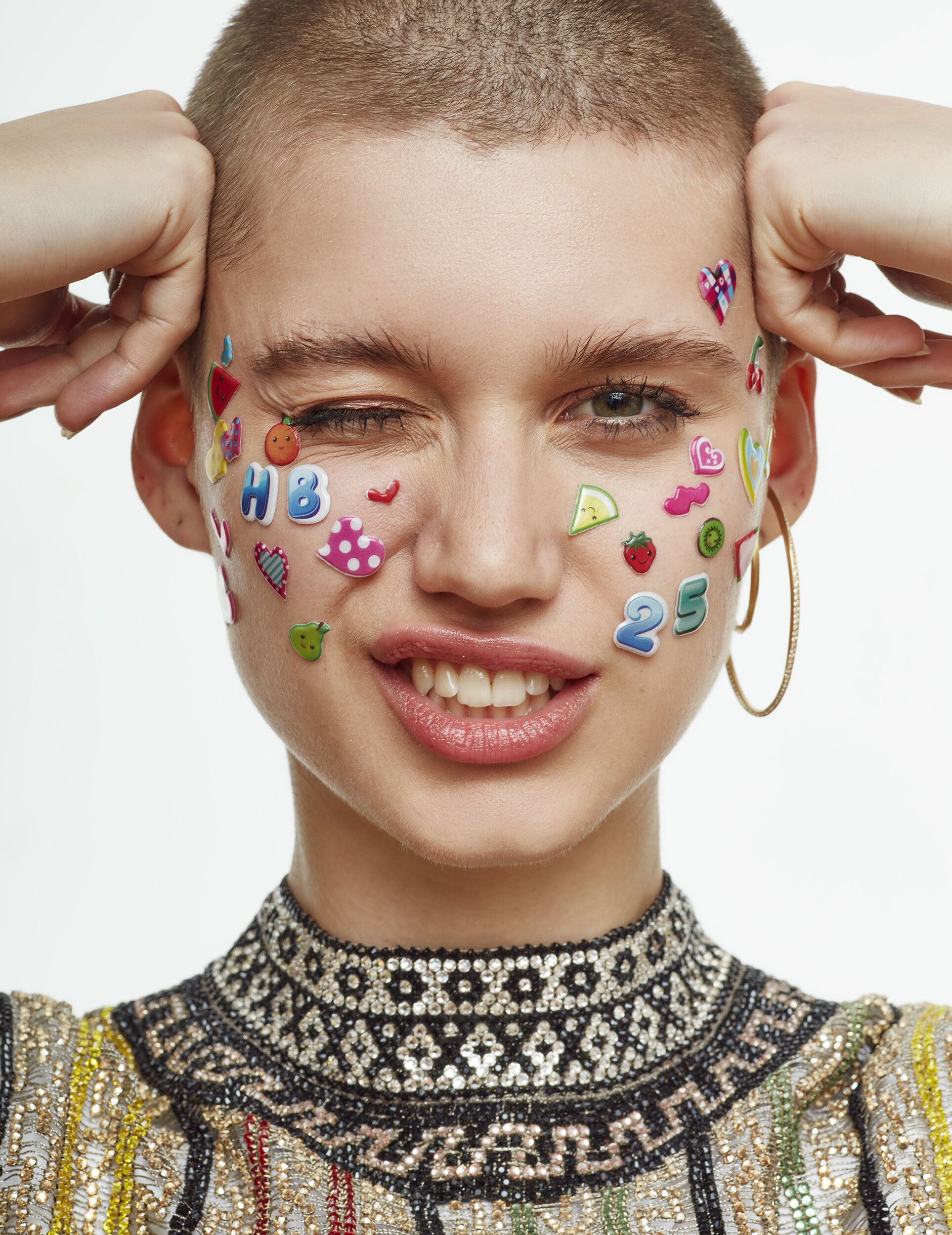 A woman with short hair and large hoop earrings, with colorful stickers on her face, winking and smiling.