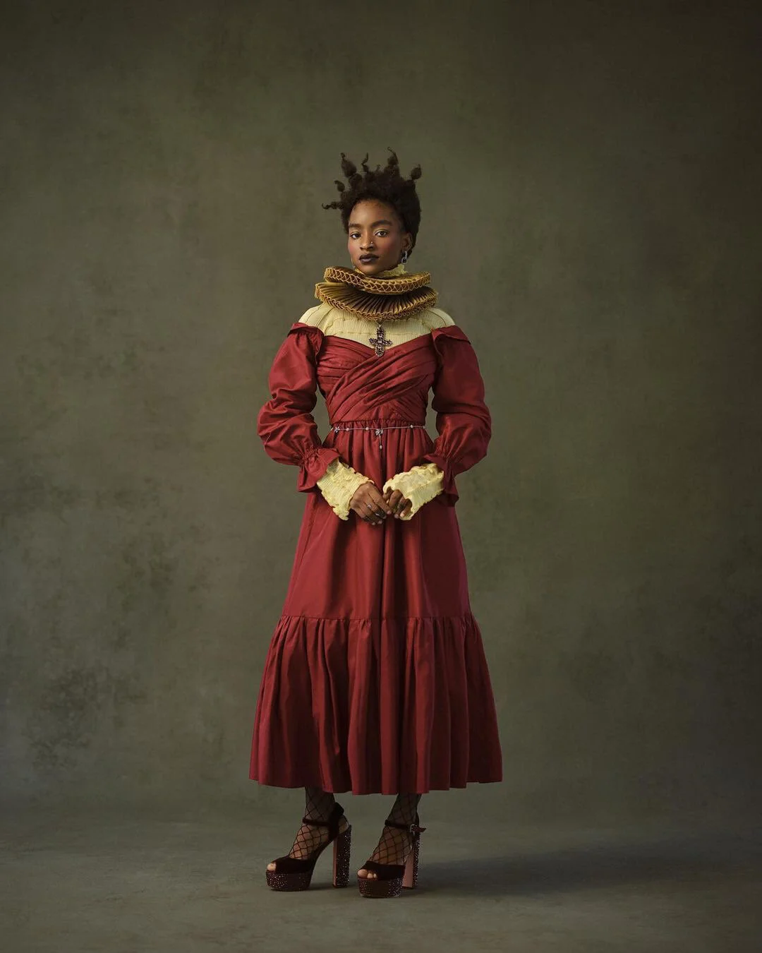 A woman wearing a vintage-inspired red and beige dress with puffed sleeves, lace gloves, and high platform heels, standing against a plain background.