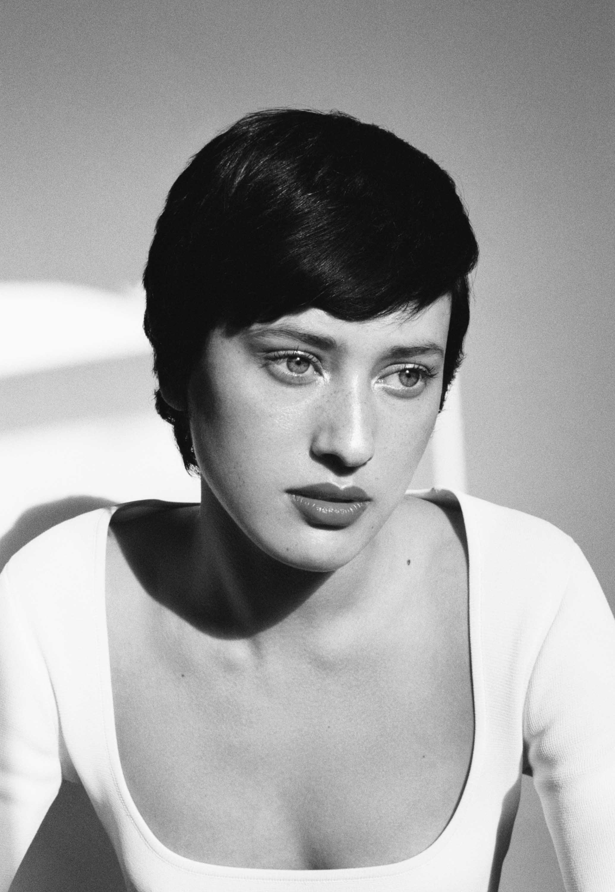 A black and white close-up photograph of a woman with short dark hair, wearing a white top, looking to her right.