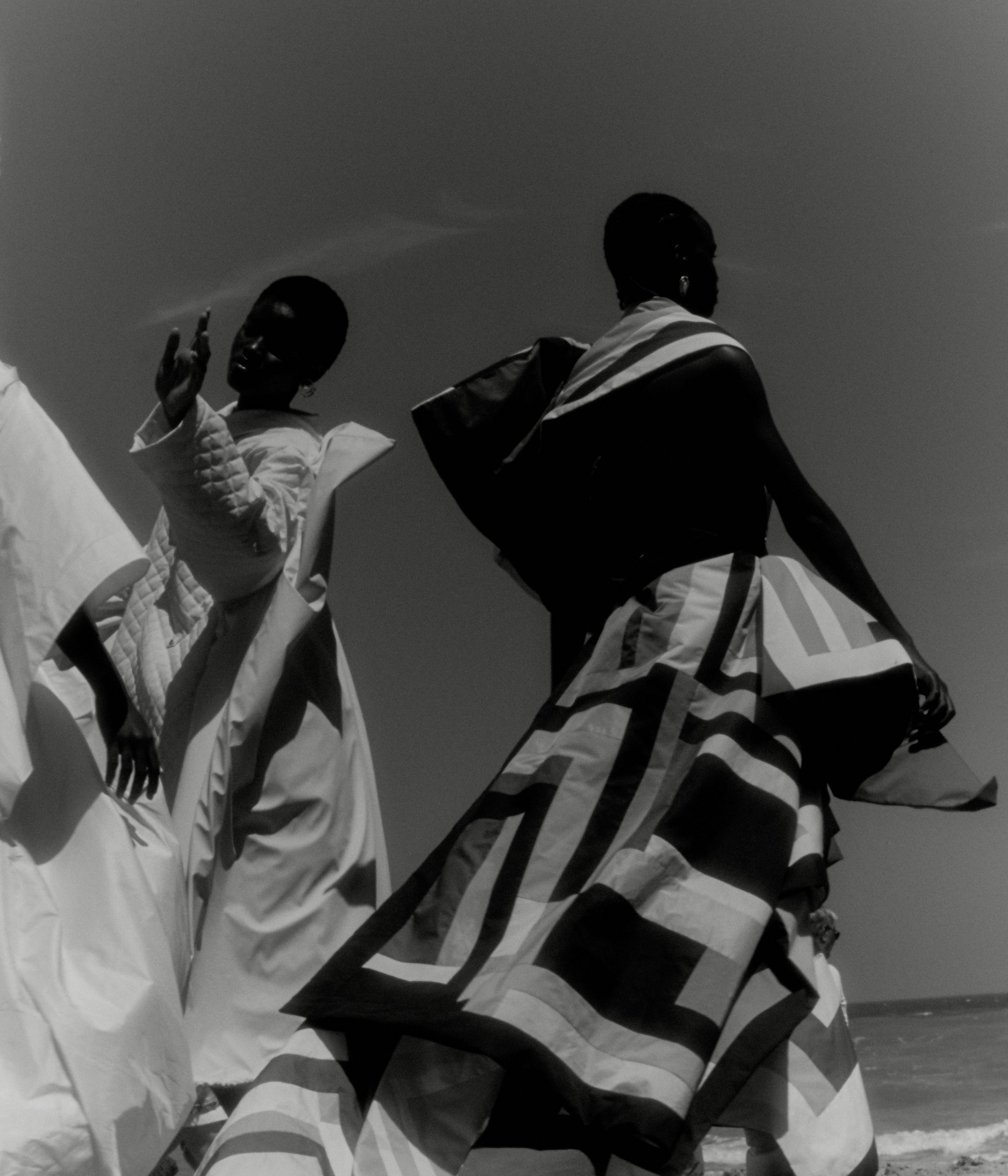 Two women dressed in traditional African clothing, standing outdoors against a clear sky.