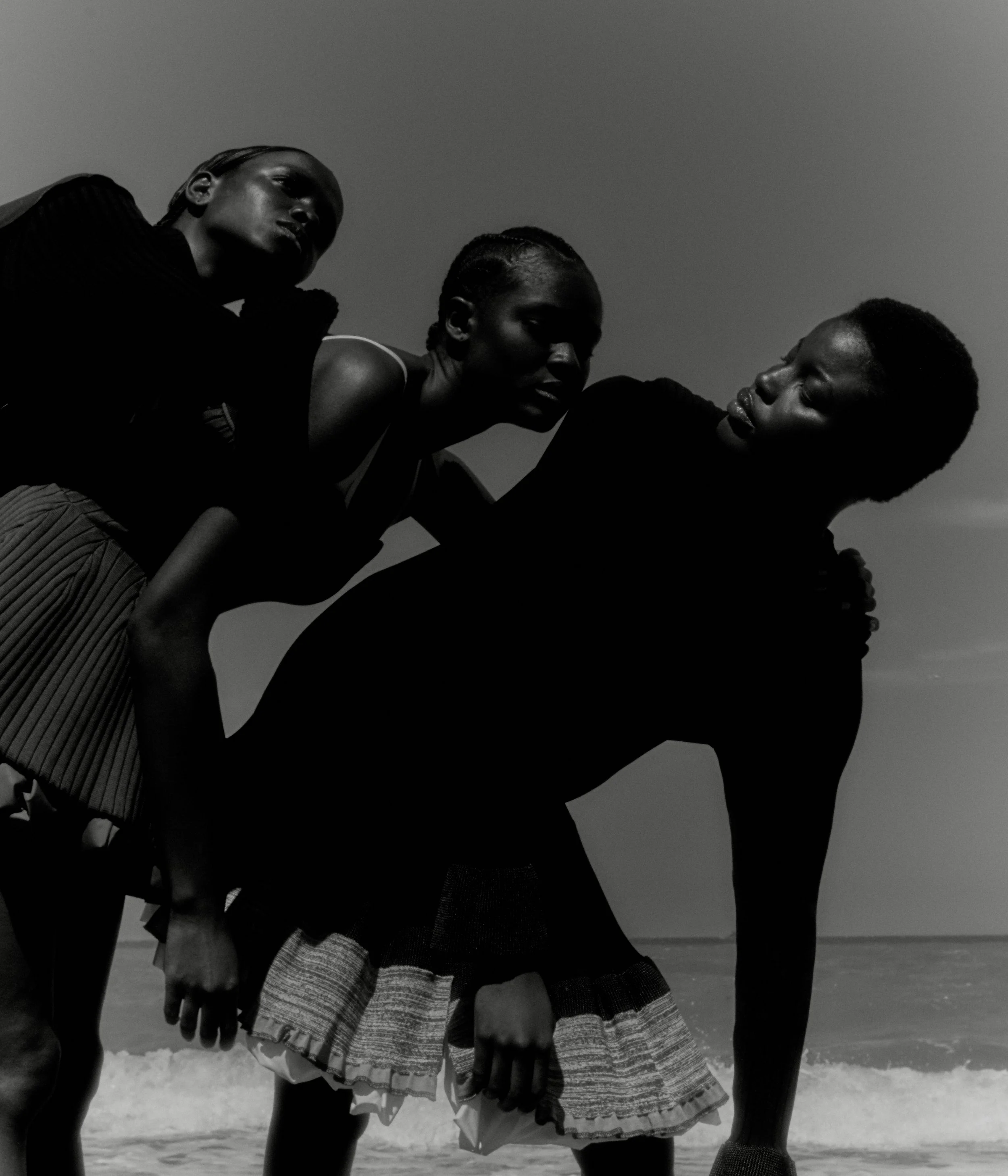 Three people holding each other on a beach, with the ocean and sky in the background, in black and white.