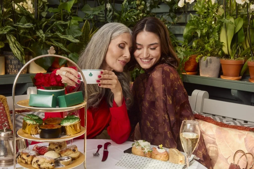 Two women enjoying an afternoon tea party with pastries, cookies, and a glass of champagne at the Ivy