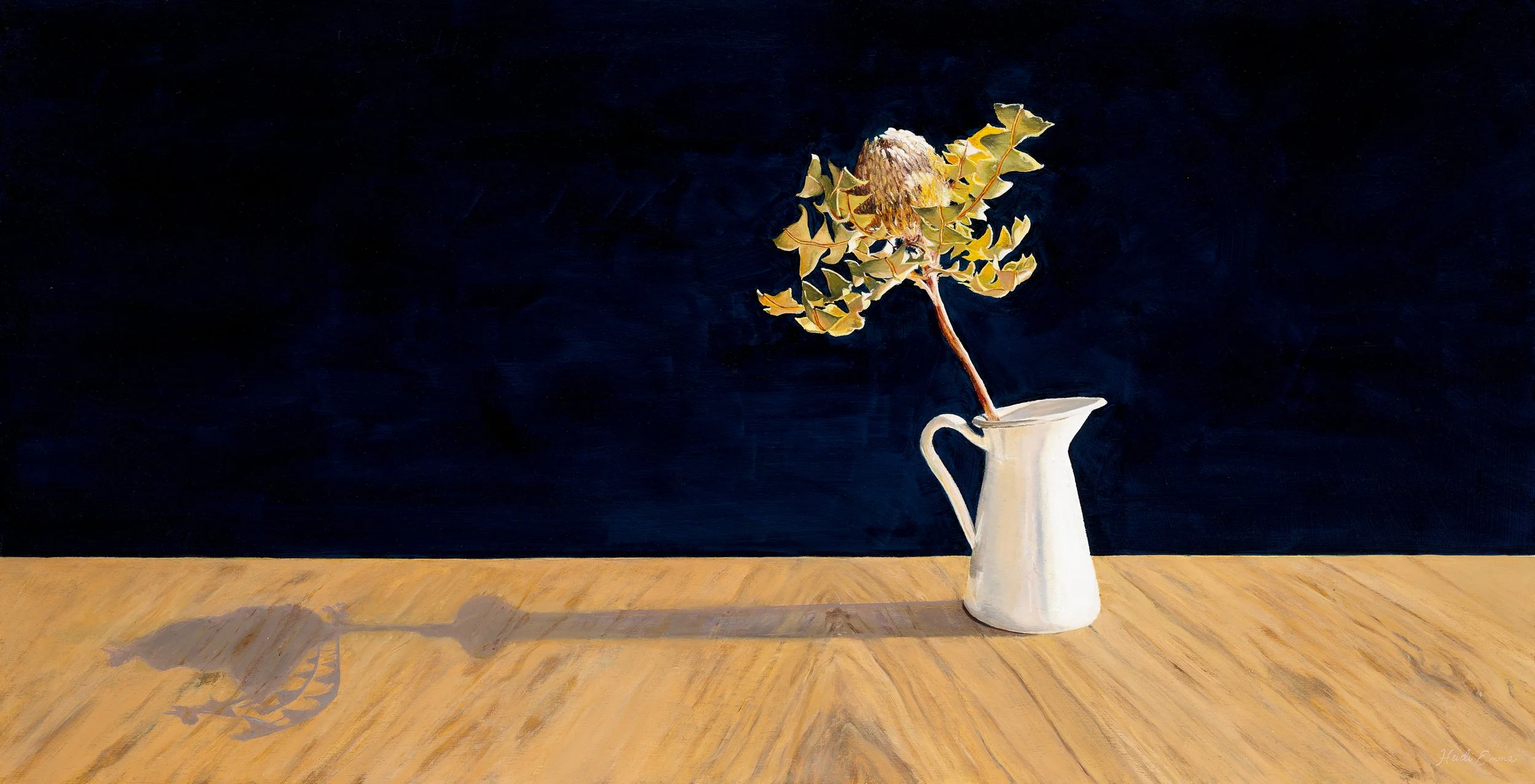 Standing in the Sun has a dramatic dark blue background oak table top and brilliant morning light casting a long shadow behind a white enamel jug with a single banksia flower
