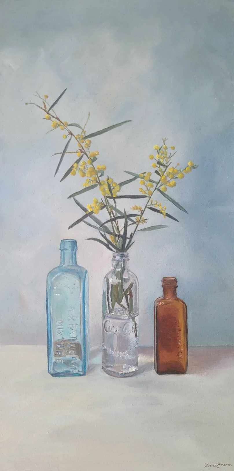 In Your Presence fine art print by Heidi Emma featuring golden Australian wattle arranged with three vintage blue, clear and amber glass bottles.