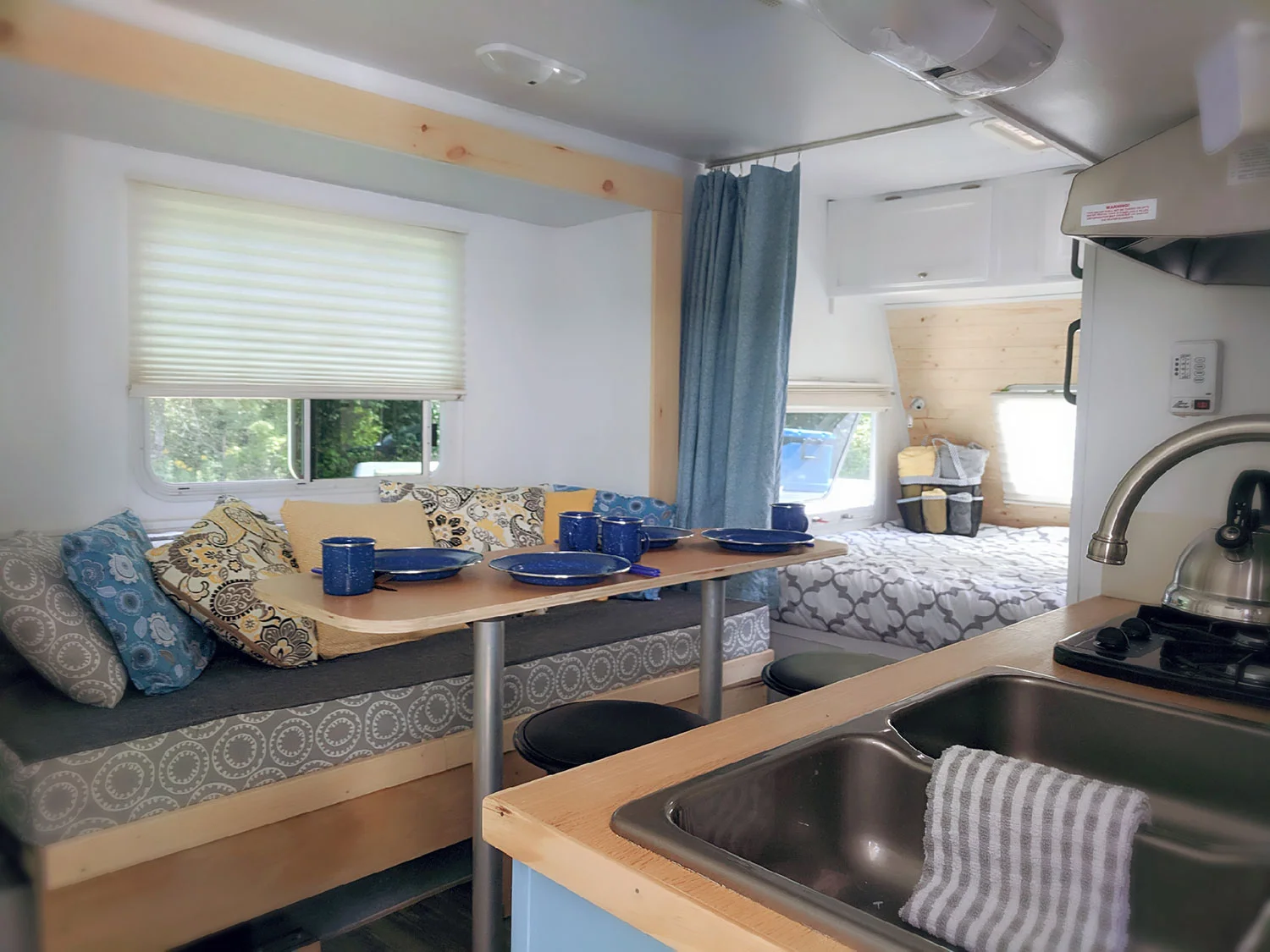 An interior shot of the Huxley, showcasing the dining area that converts into a bed measuring approximately 4½ feet x 6 feet, with a peek of the queen bunk and galley kitchen.