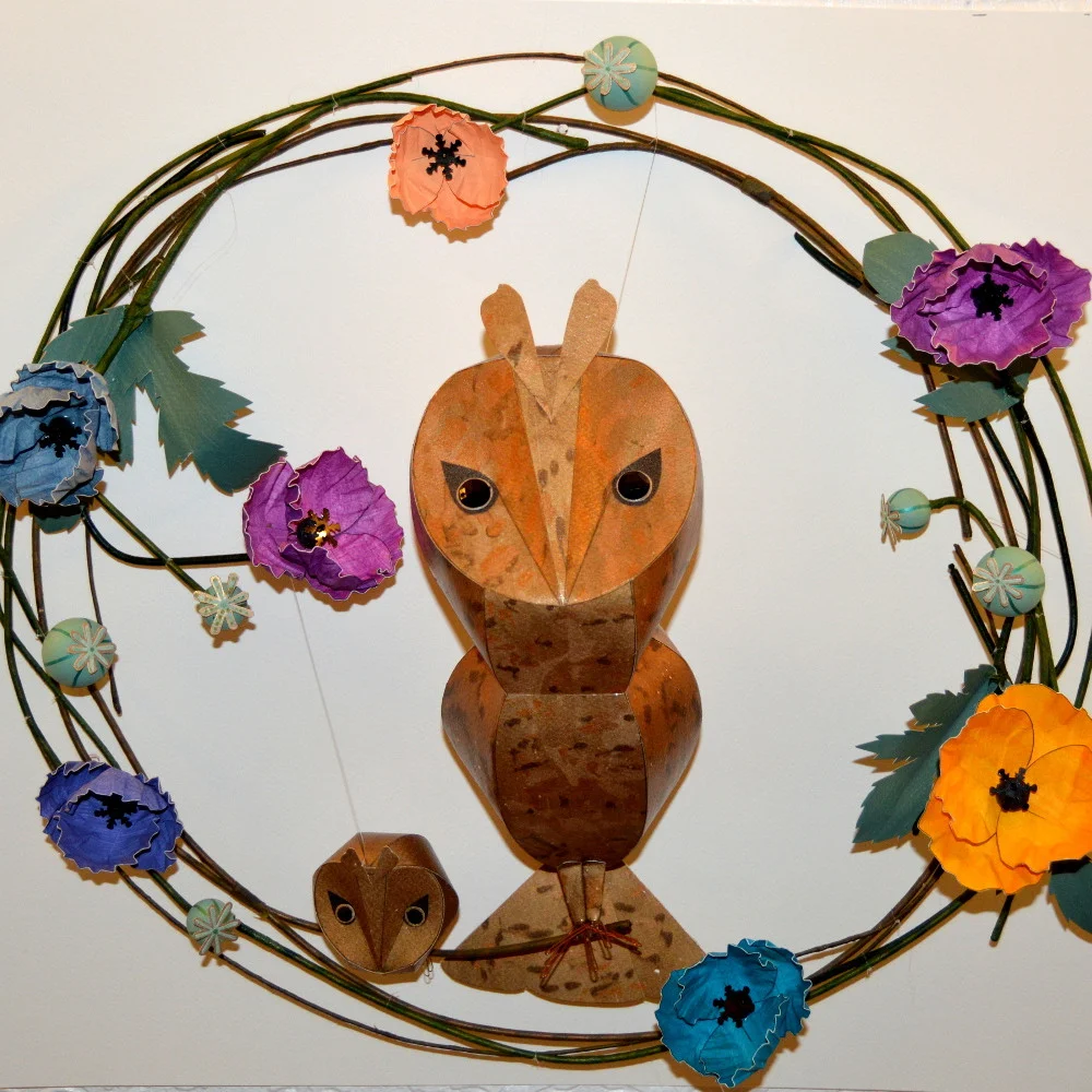 Bastian and baby Bux, perched on a multicoloured poppy wreath
