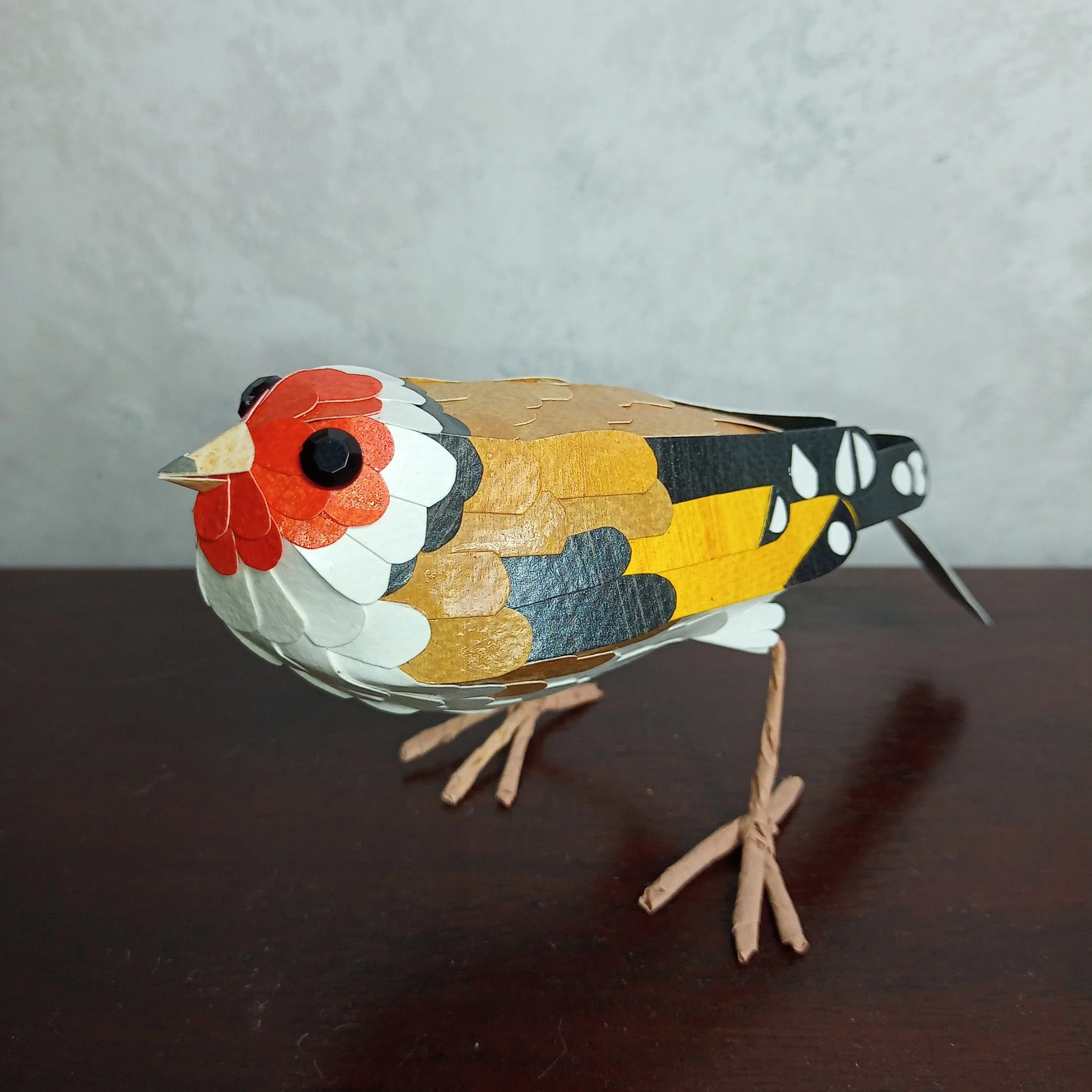 A handmade paper sculpture of Allen's hummingbird, perched on a floral wreath. Kaper