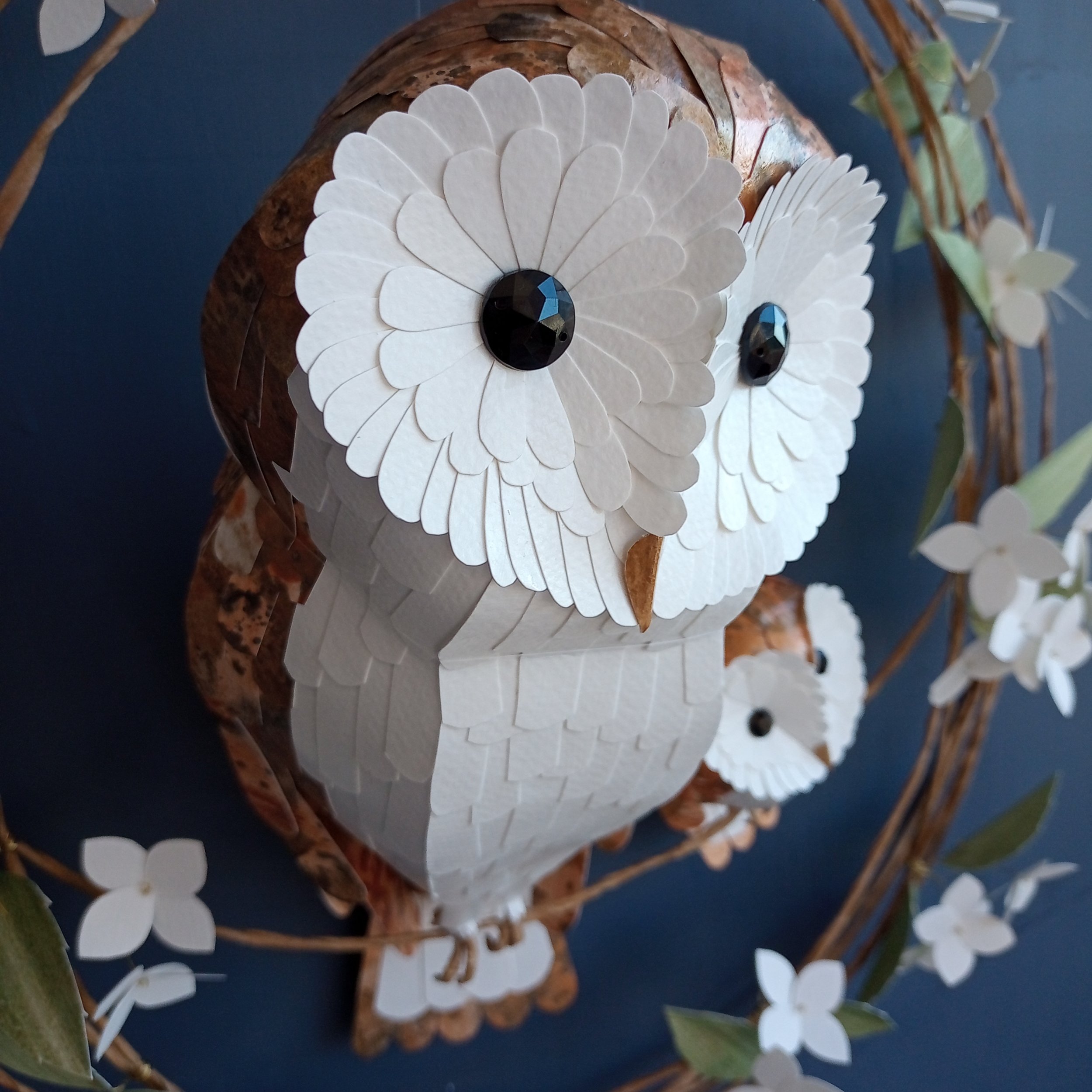 close up of a handmade barn owl sculpture, made from hand printed papers. You can see the hand cut feathers on her love heart shaped face.