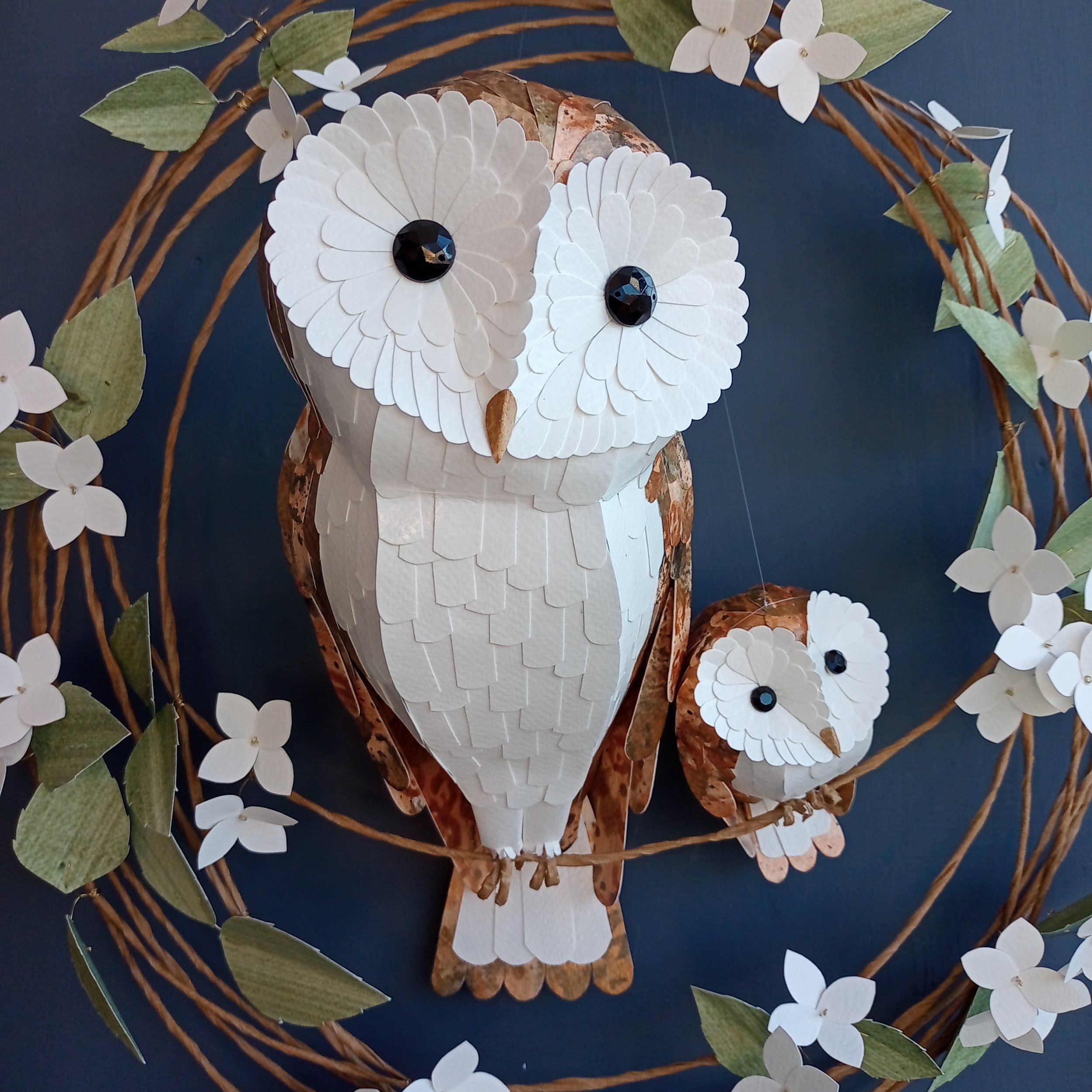 Owl themed wall décor, handmade by Kaper. This bespoke paper sculpture features a mama and baby barn owl perched on a wreath festooned with white hydrangea blooms