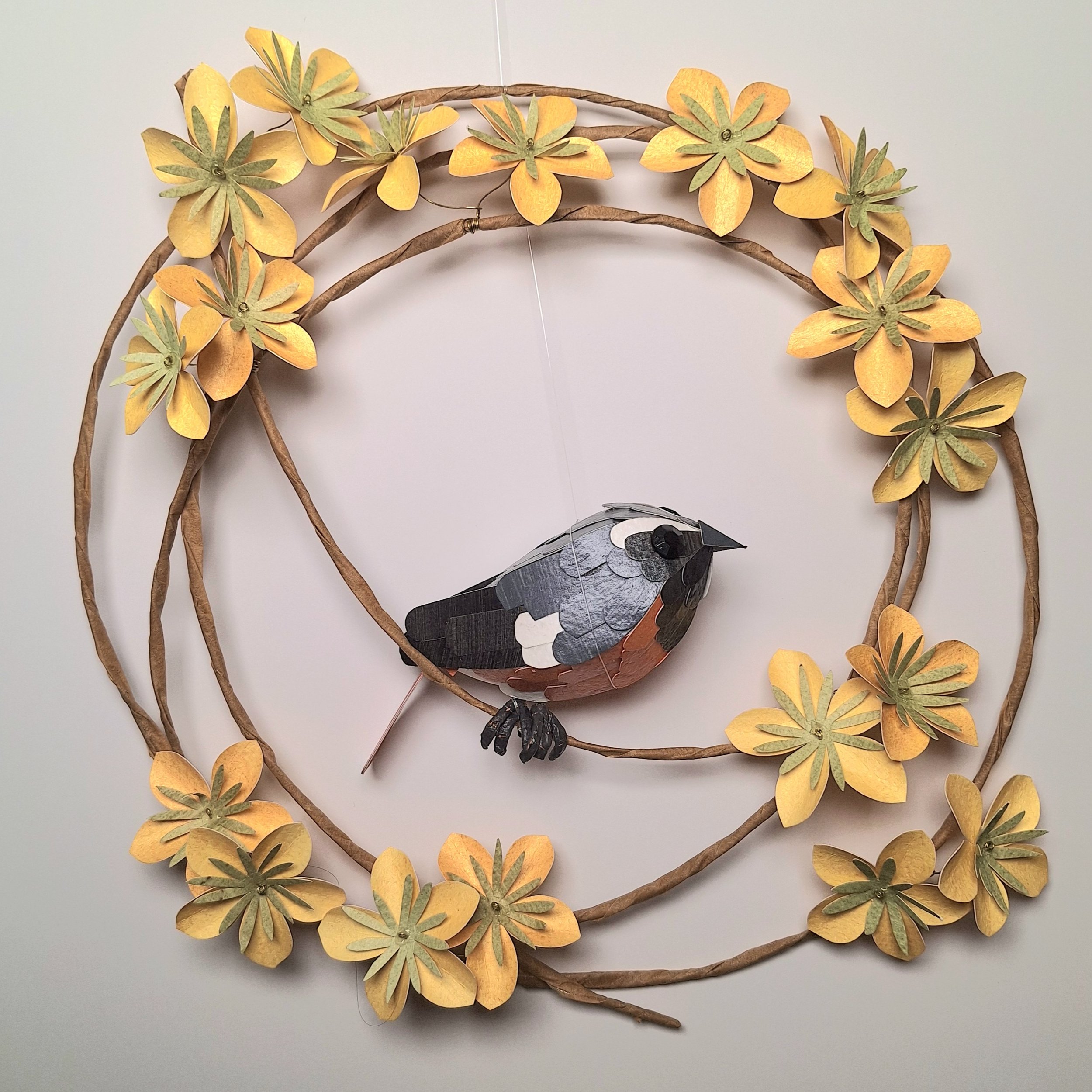 handmade paper sculpture of a redstart bird on a wreath of yellow flowers
