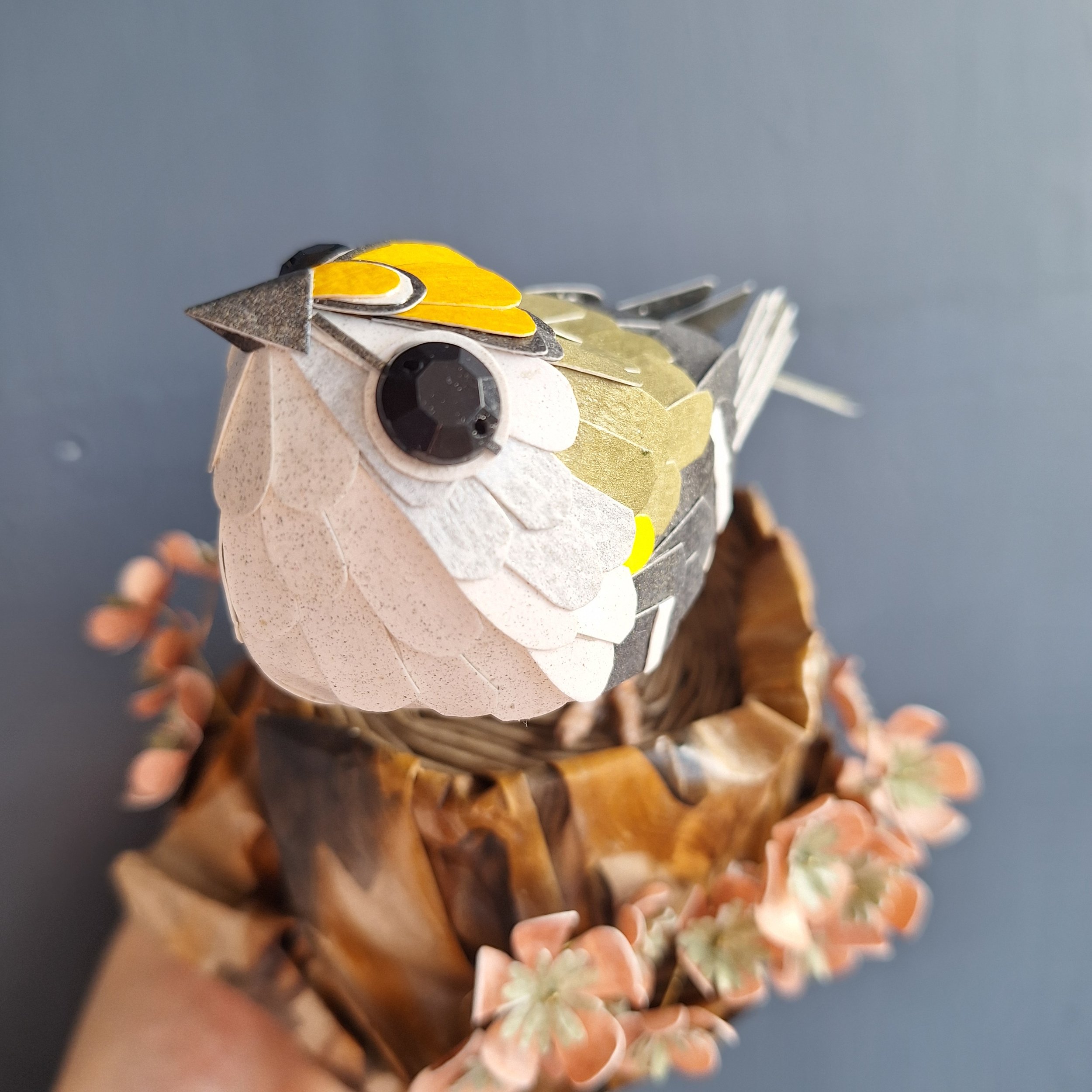 handmade paper sculpture featuring a small garden bird, the goldcrest, perched on a tree stump